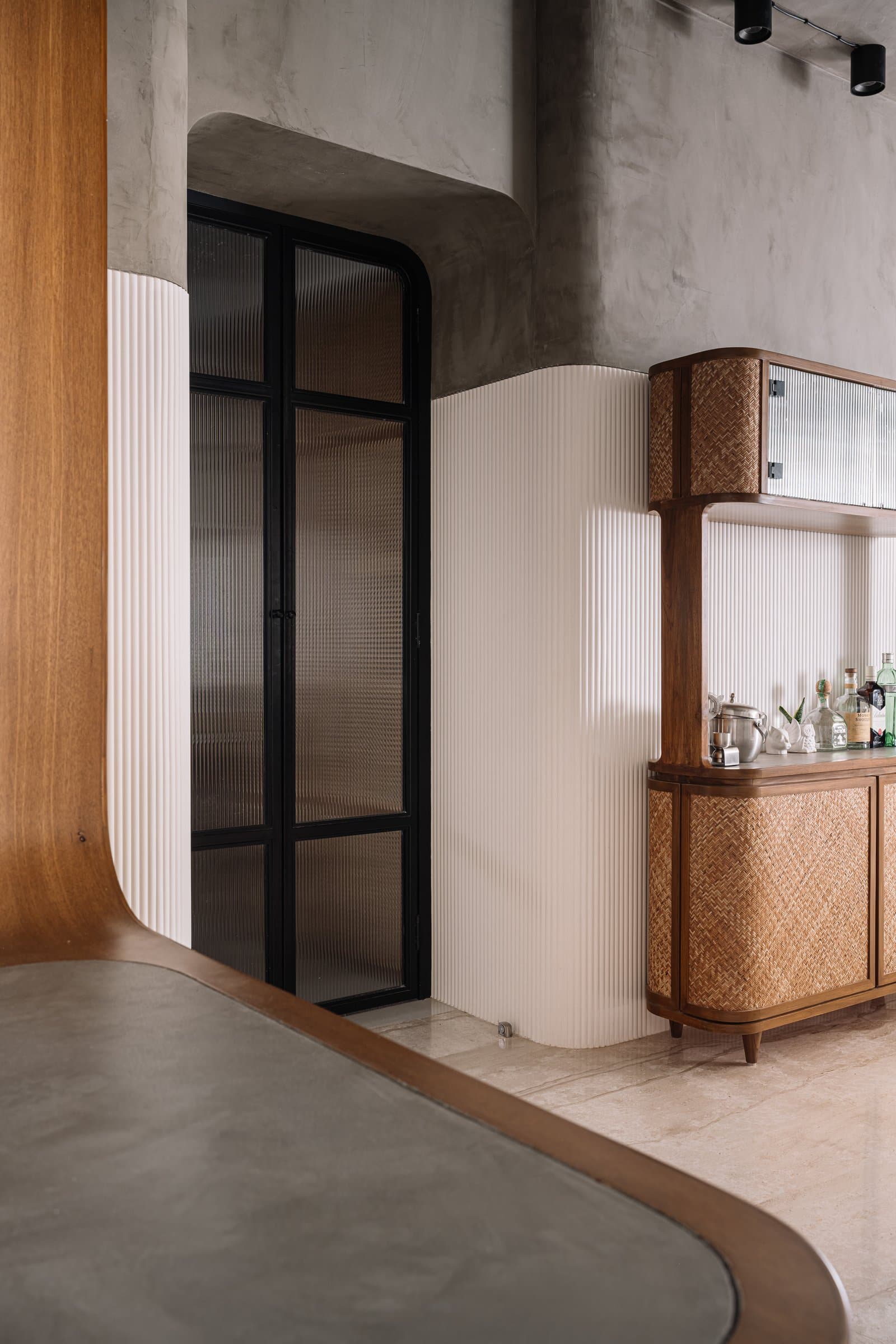 The kitchen threshold: a black-framed fluted glass door set within sinuous white panelling, the bar unit beside it