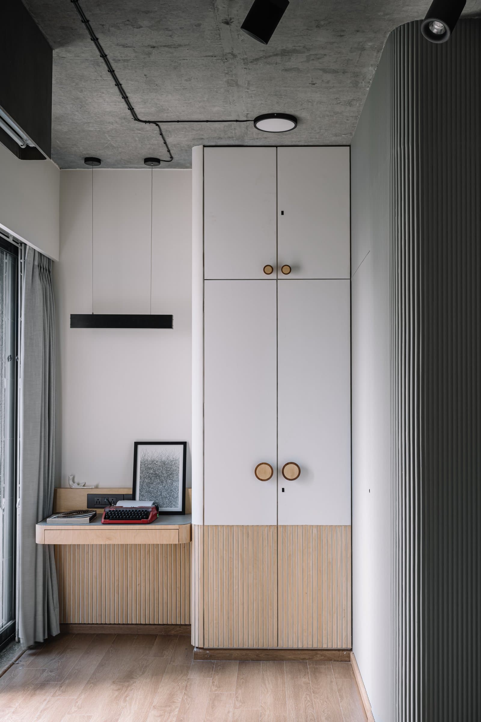 The master bedroom's study corner, pale timber and circular hardware against the exposed concrete ceiling