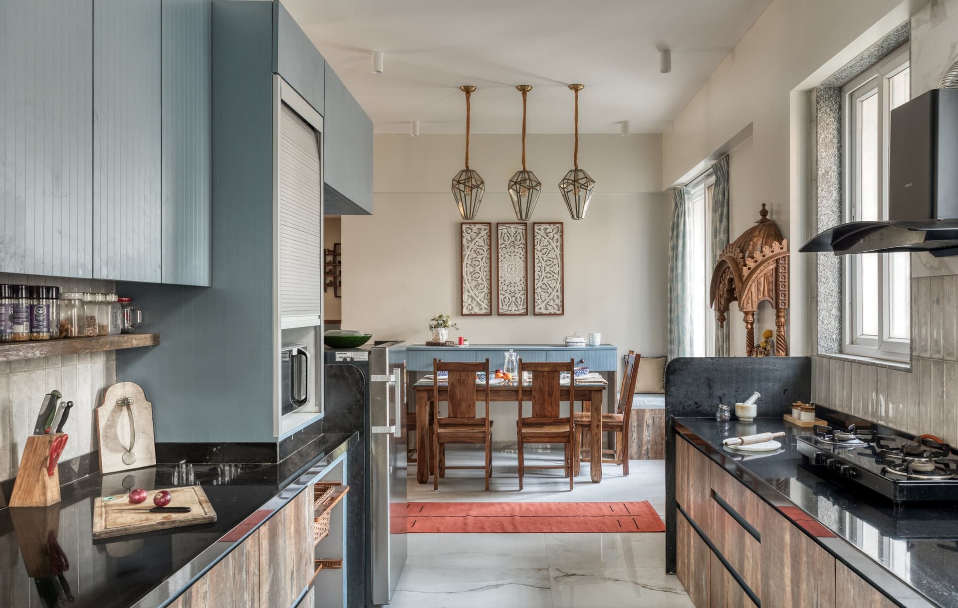 Kitchen and dining viewed as a single sightline, unified by soft blue cabinetry and geometric brass pendants