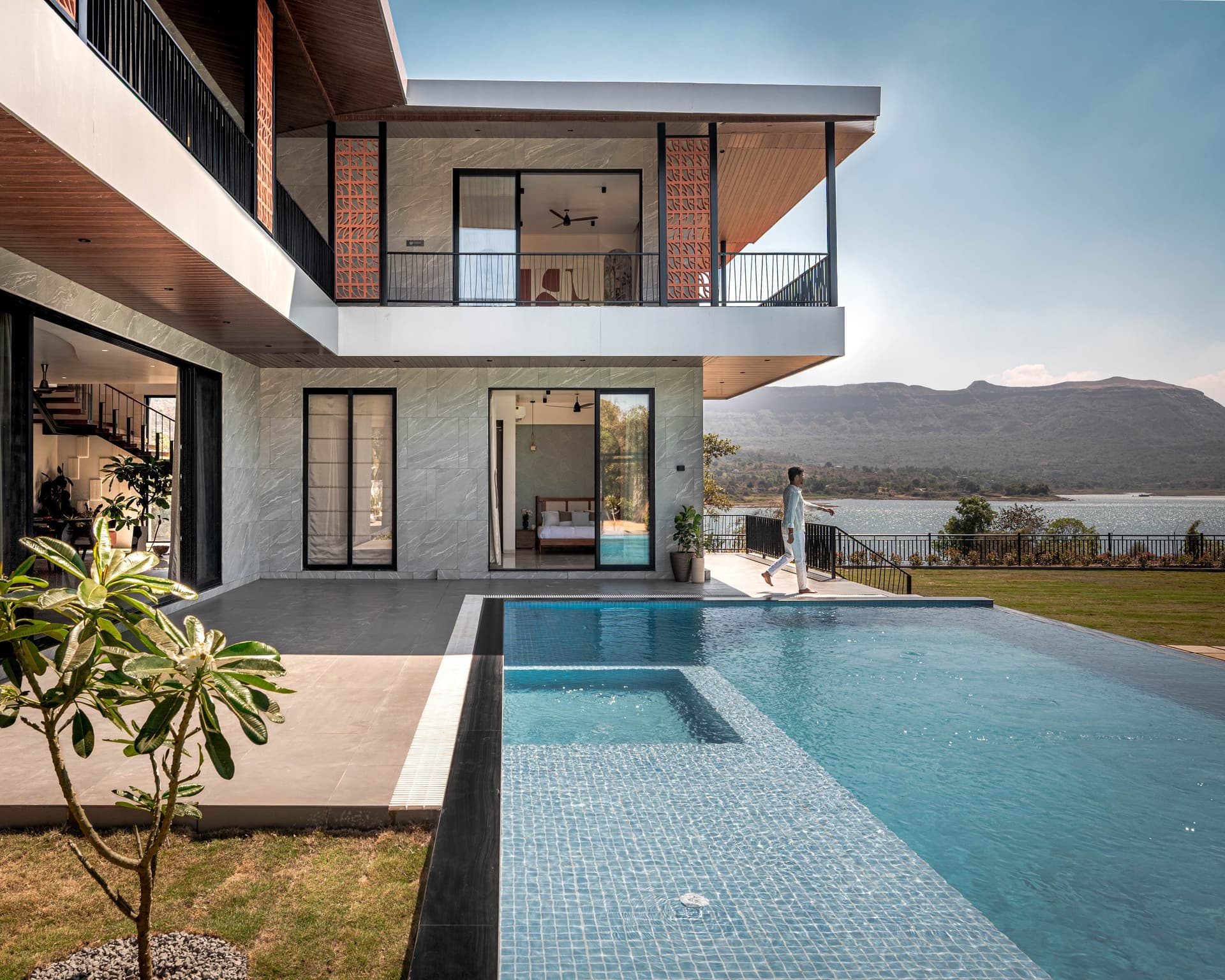 The villa from the garden: steel frame, stone cladding, terracotta screens, and the pool extending toward the reservoir