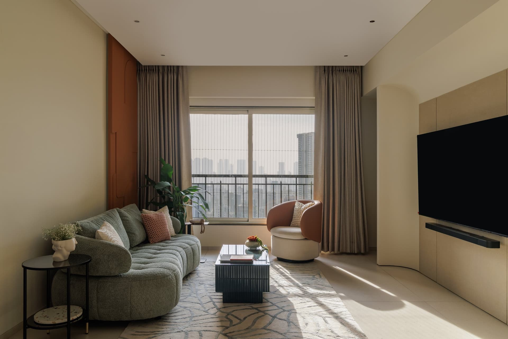 In the living room, a sage boucle sofa faces a wall of sculpted burnt sienna; every form curves