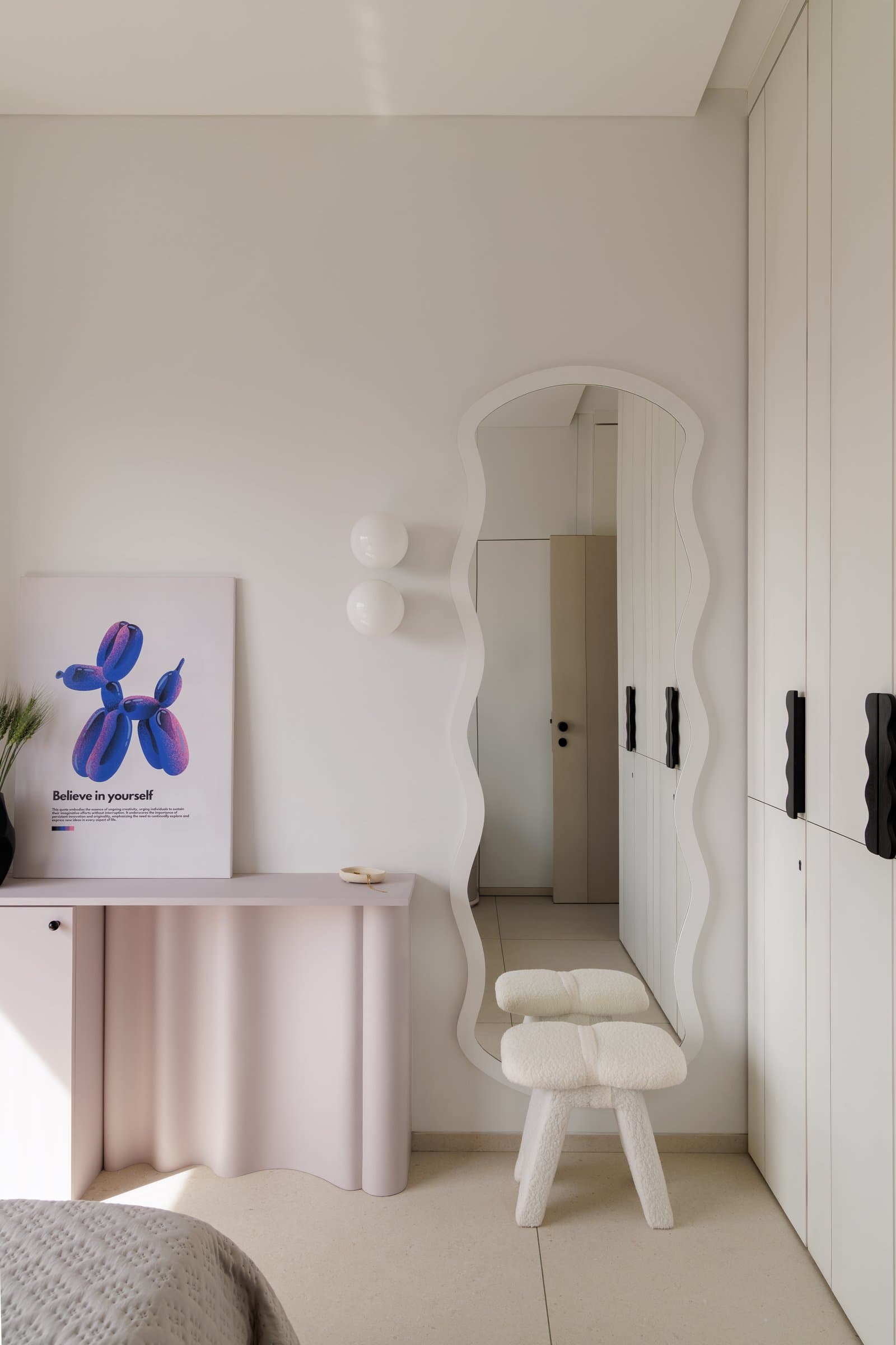 A wavy-edged mirror and undulating blush console anchor the dressing corner