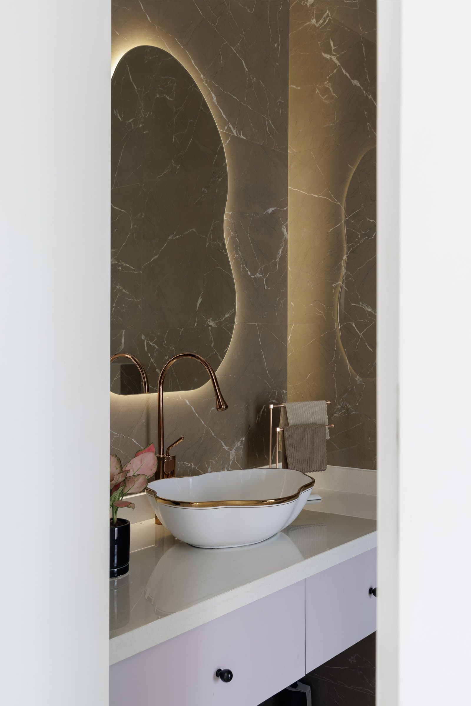 The daughter's powder room, where a backlit pebble mirror and a scalloped basin earn their indulgence