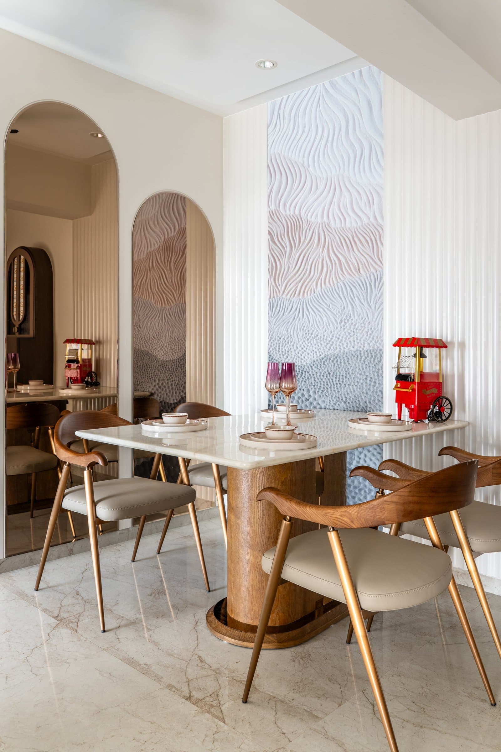 The dining area, where the dune metaphor turns literal: a rippled plaster panel between fluted columns, paired with walnut wave-back chairs