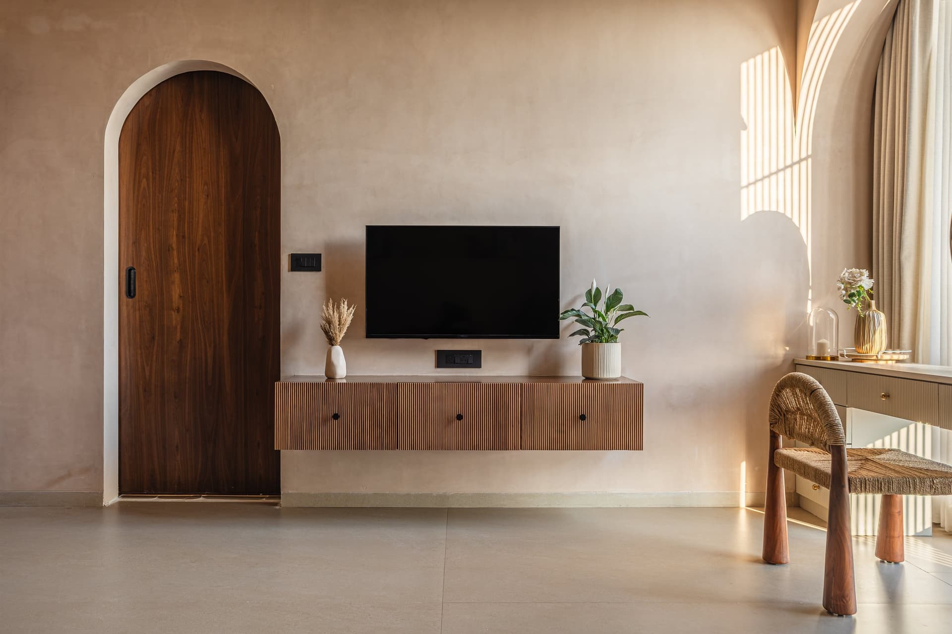 An arched timber door and fluted console anchor the master wall as slow shadow lines move across the plaster