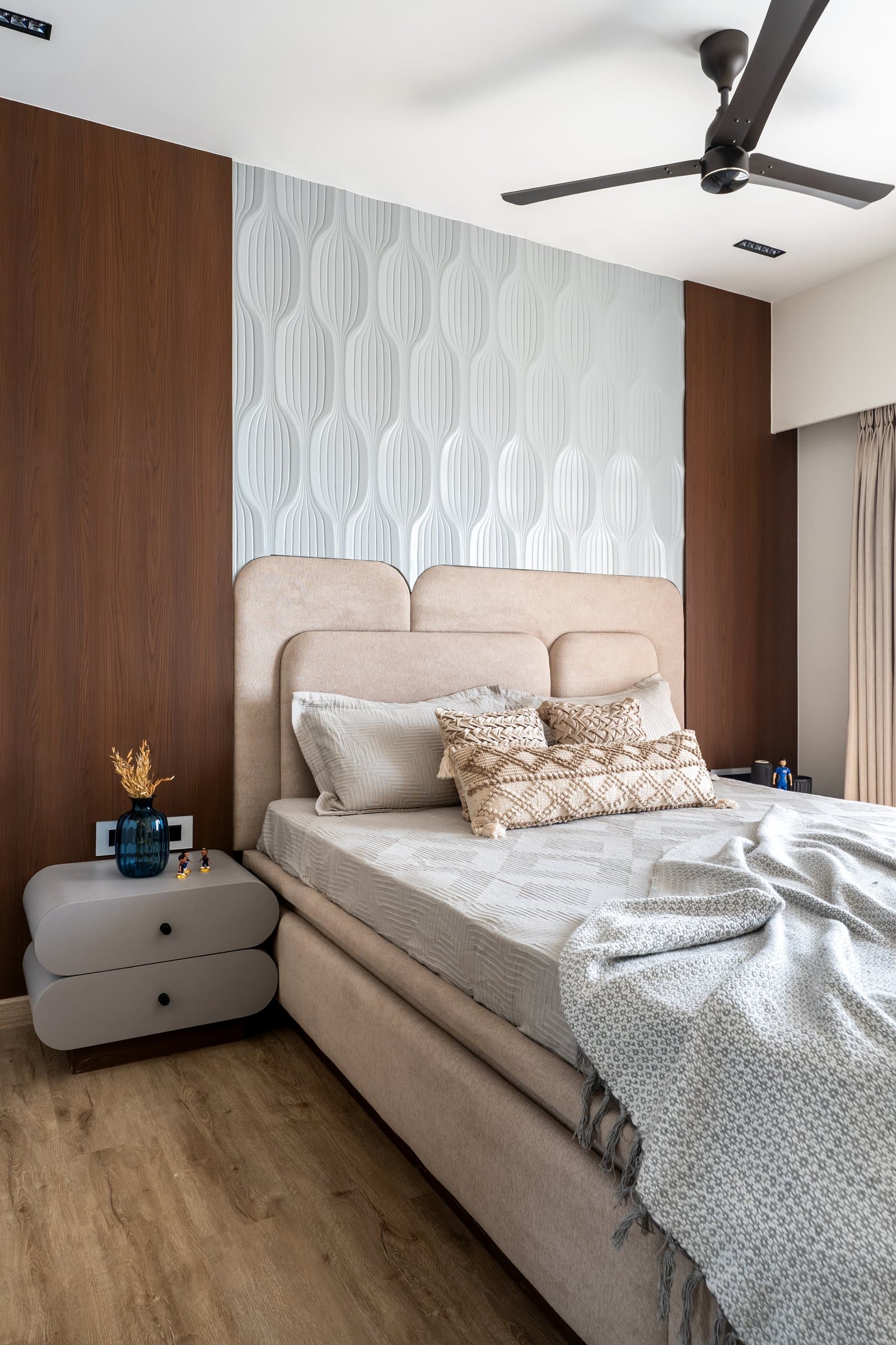 In the first bedroom, walnut flanking panels frame a wall of pale leaf-motif wallpaper above a low suede headboard