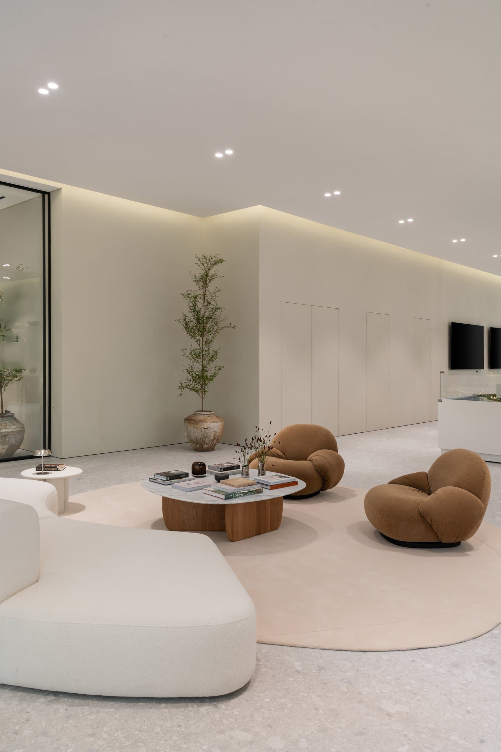 The first guest seating hub: camel-toned Gubi Pacha chairs and a curved cream sofa gathered around a marble-and-oak table