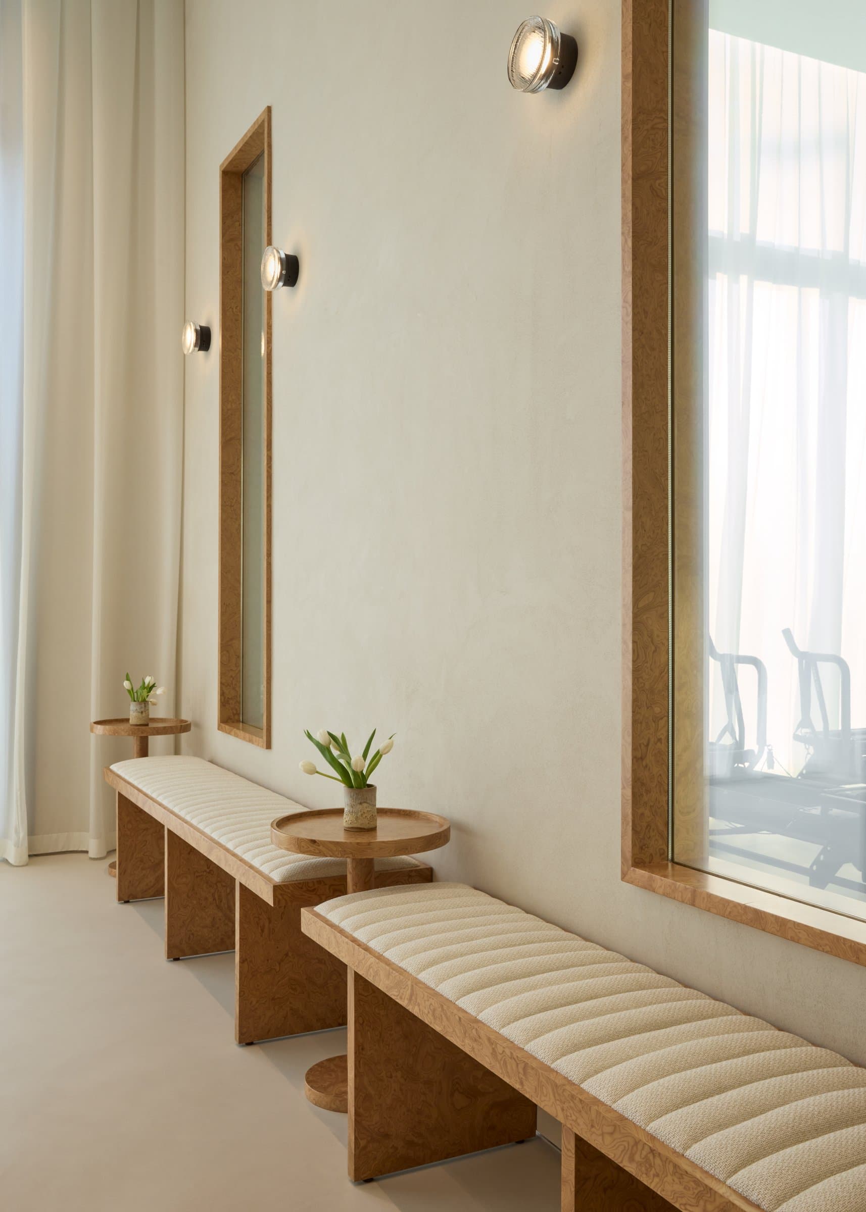 A run of burl wood benches lines the corridor outside the Lagree studio, with Marset sconces punctuating the micro-cement wall