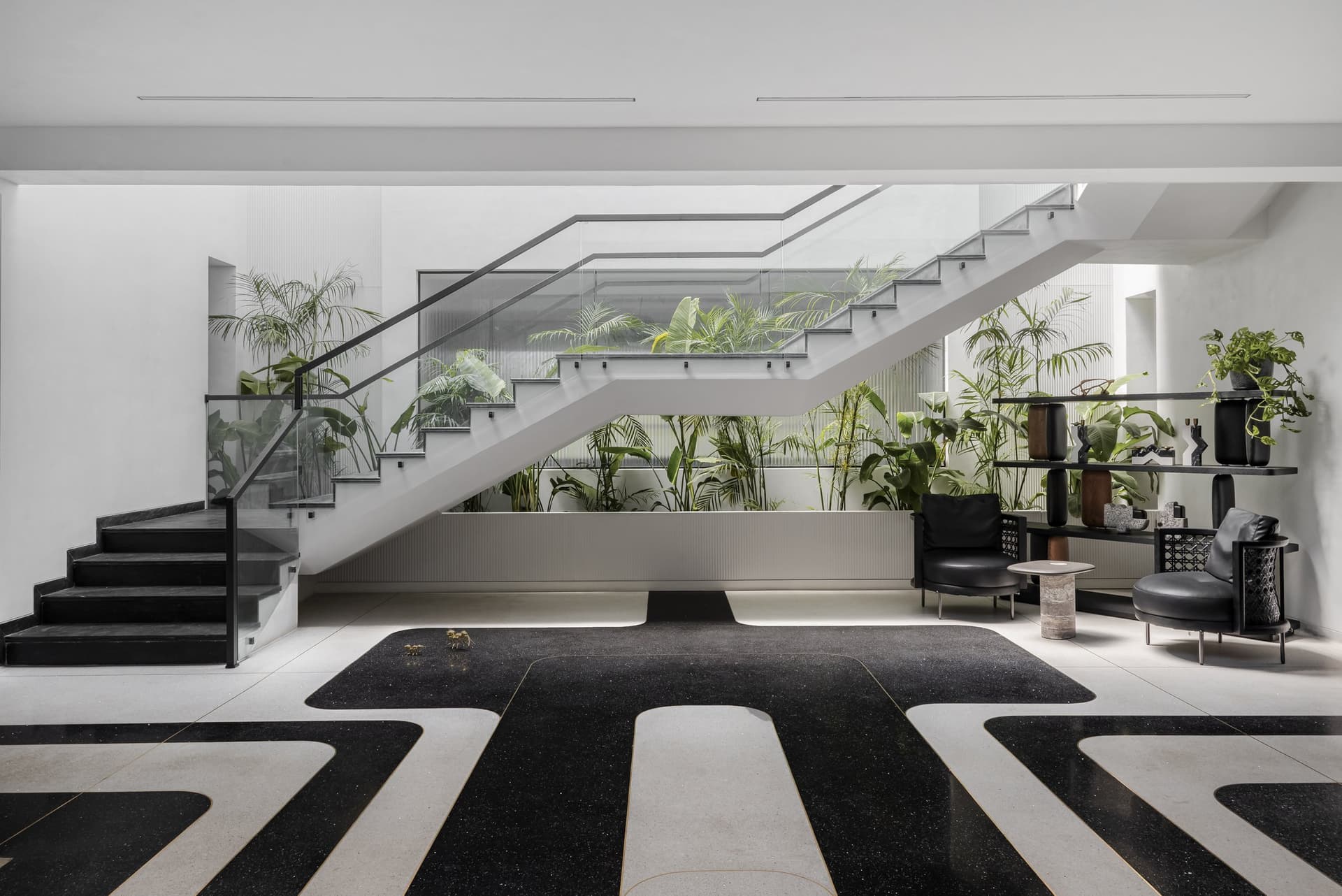 The double-height foyer, where a graphic terrazzo floor and a glass-balustered staircase set the home's spatial language
