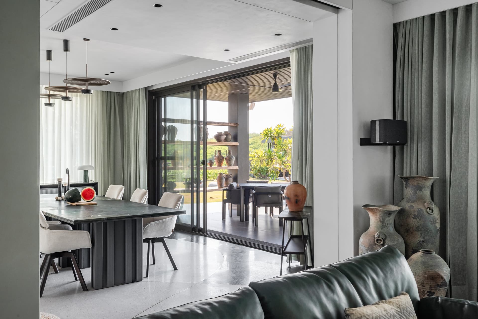 The dining zone flows from the living room, with weathered vessels marking the threshold to the outdoor terrace