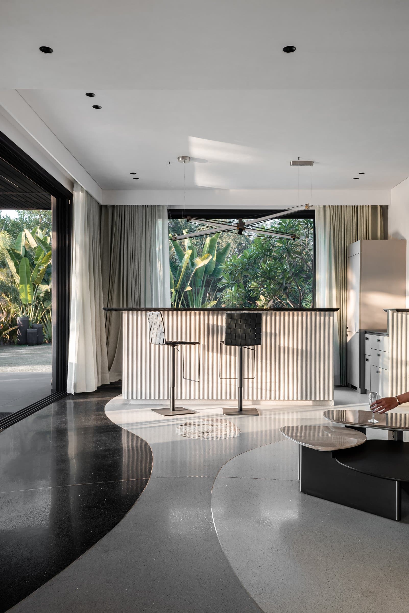 A backlit bar counter sits against another wall of glazing, the garden pressed close behind