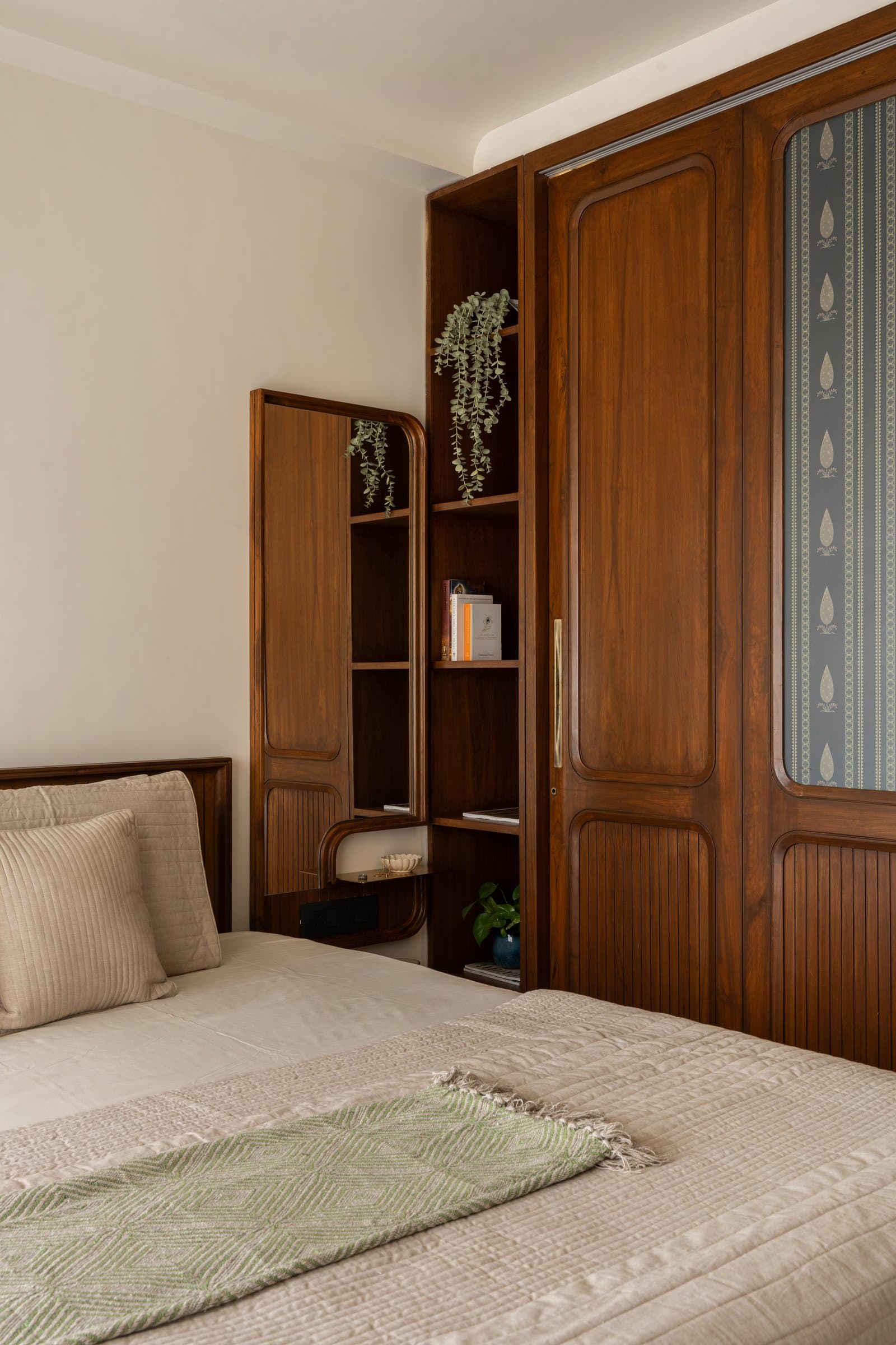 The wardrobe's panelled teak shutters carry a subtle paisley wallpaper insert, doubling as the bedroom's decorative event