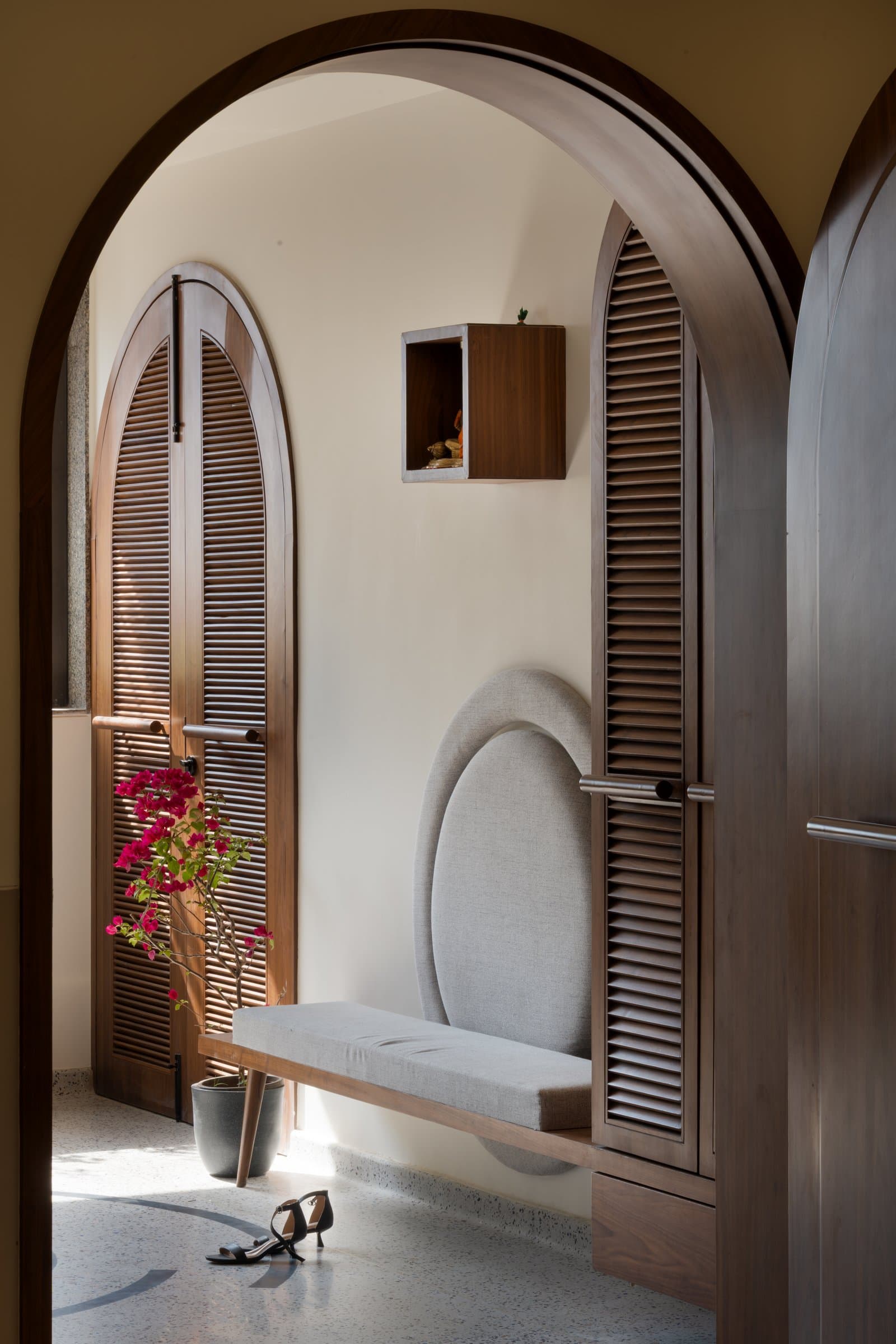 The foyer, where a walnut arch frames a louvred wardrobe wall and an oval upholstered niche
