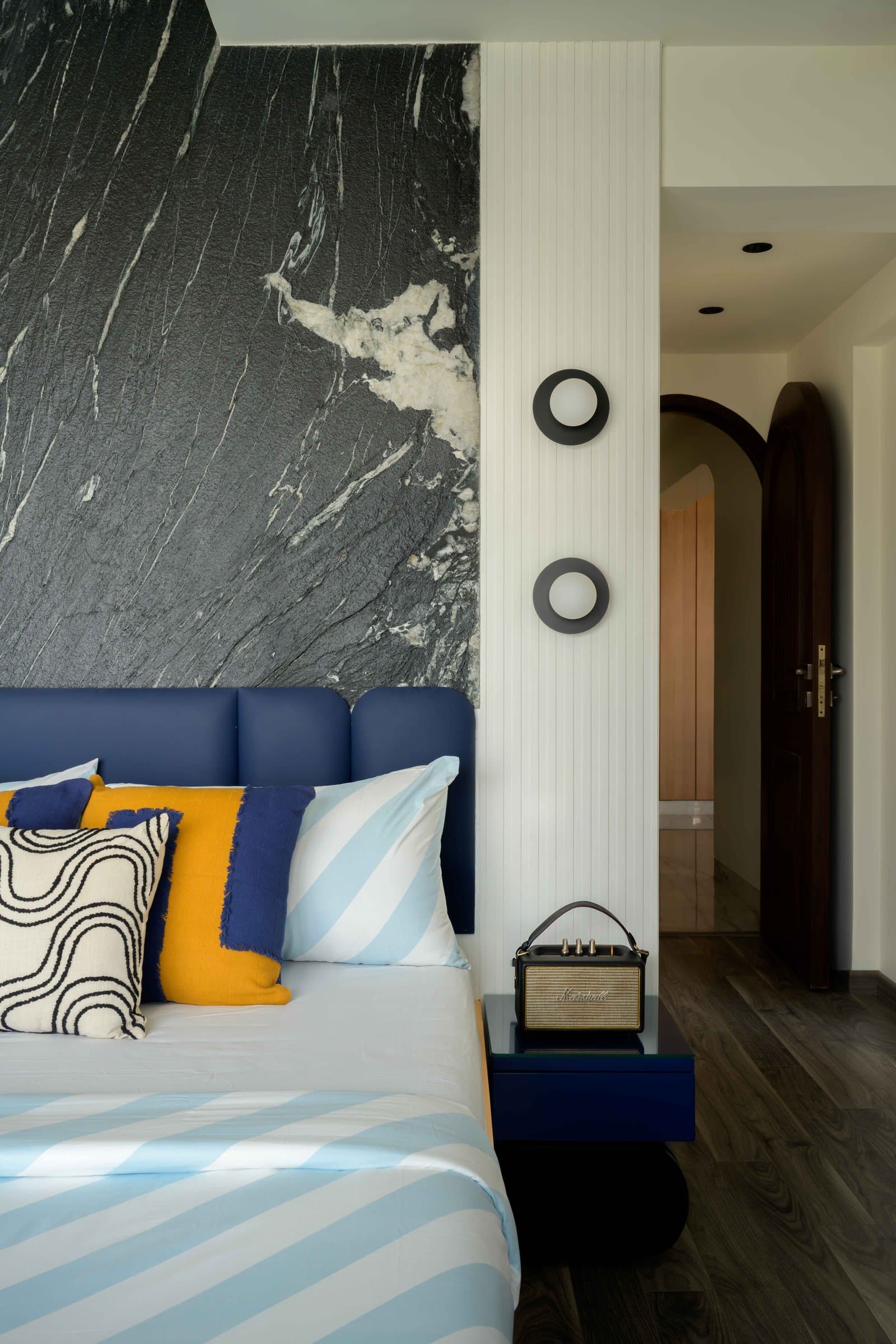 The son's bedroom, where stone, blue upholstery, and a fluted white panel hold a tight conversation
