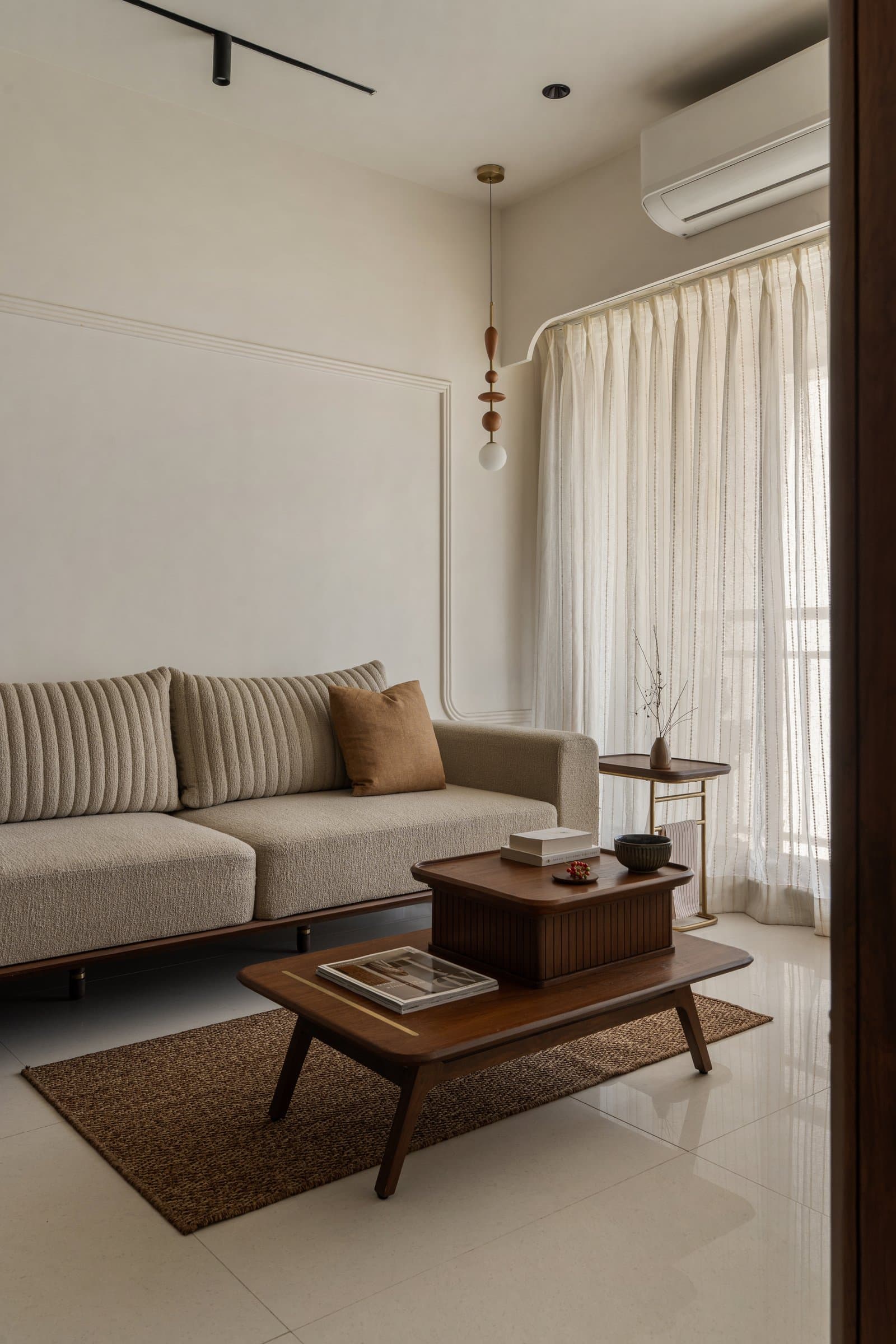 The living room, where continuous wall mouldings and a pair of nesting tables in dark teak create a hugging volume that doubles as low dining