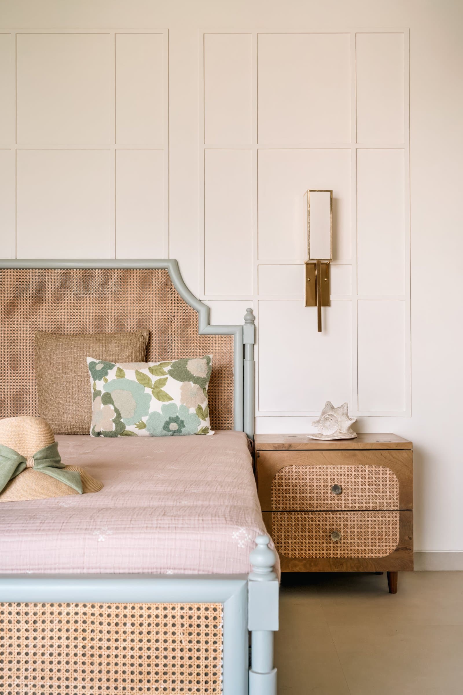 A daughter's room: pale blue cane-inset bed, full-height panelled moulding and a warm wood bedside chest with a cane drawer face