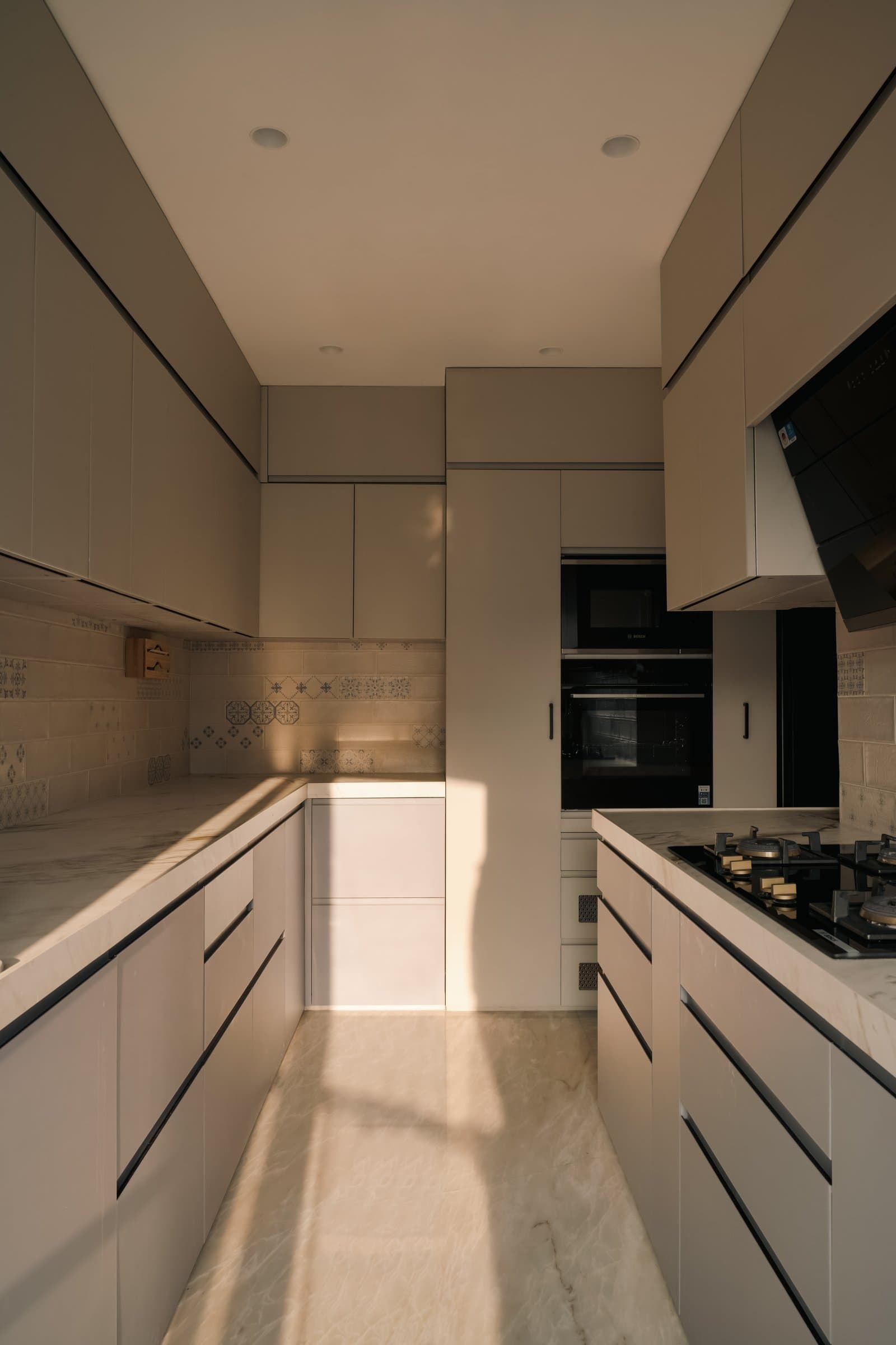 The kitchen, handleless mushroom-toned cabinetry paired with a veined stone counter and a patterned tile backsplash