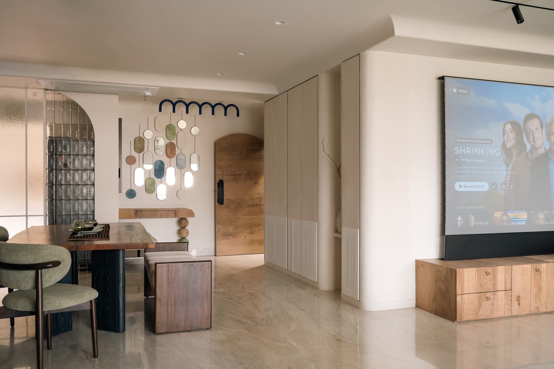 The main volume reveals the home's vocabulary: pale fluted cabinetry, an arched solid-wood door, a glass-block partition and a composition of suspended oval mirrors