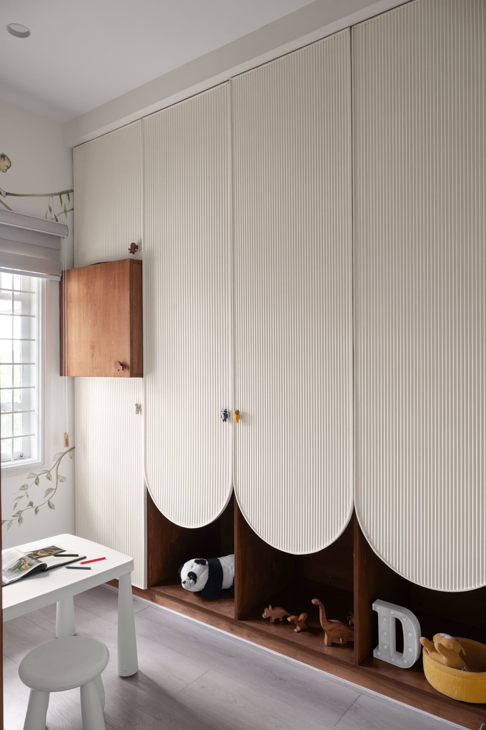 The fluted wardrobe with curved scalloped edges and an open plinth sized for small hands and softer landings
