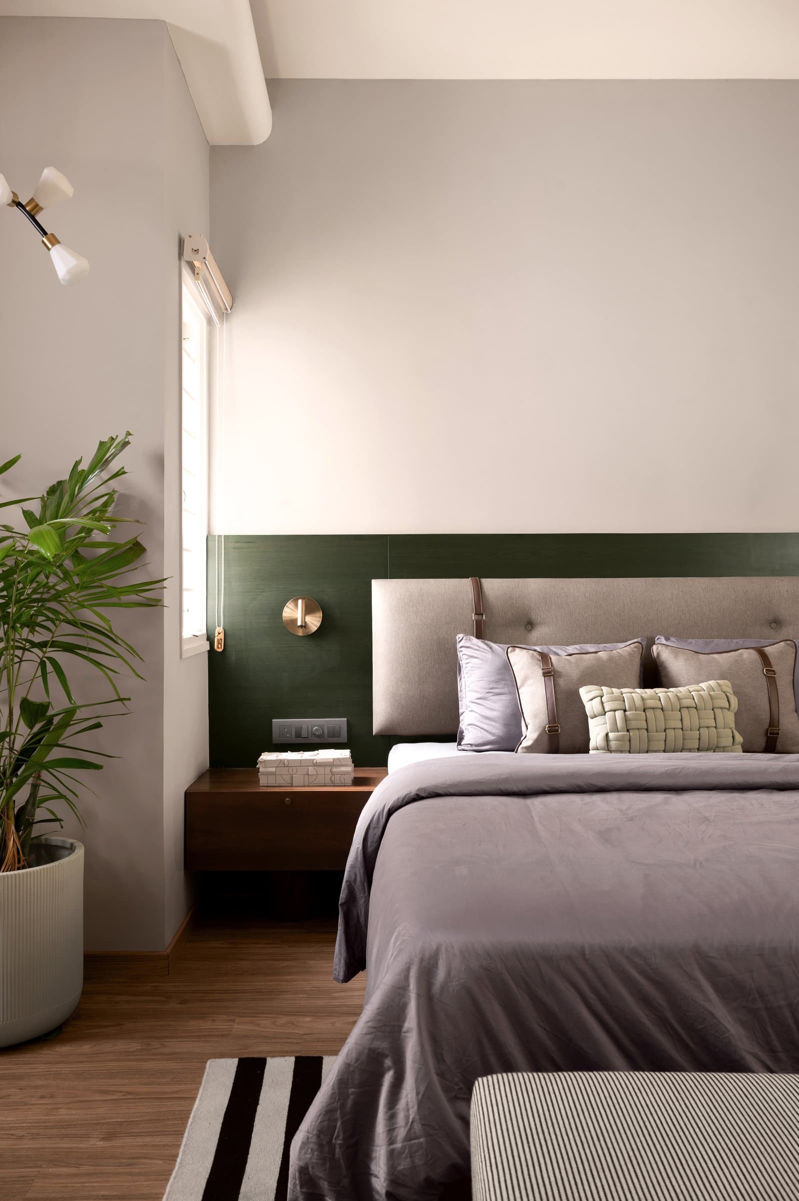 A side view of the primary bedroom, with a slim window breaking the green panel and a brass sconce for reading