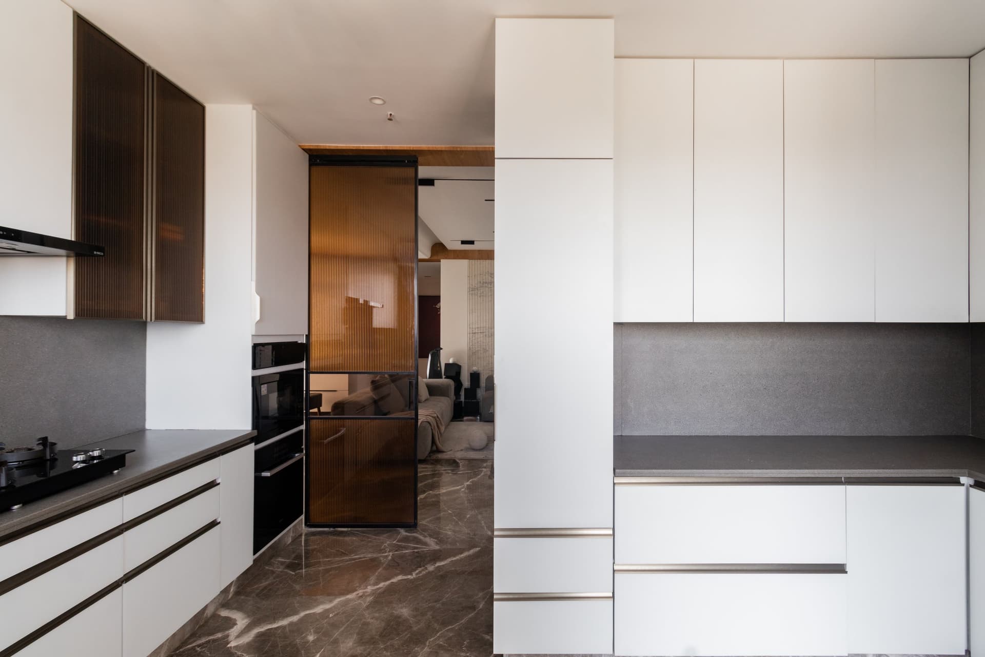 The kitchen threshold, where a sliding amber reeded-glass door preserves continuity with the social zones