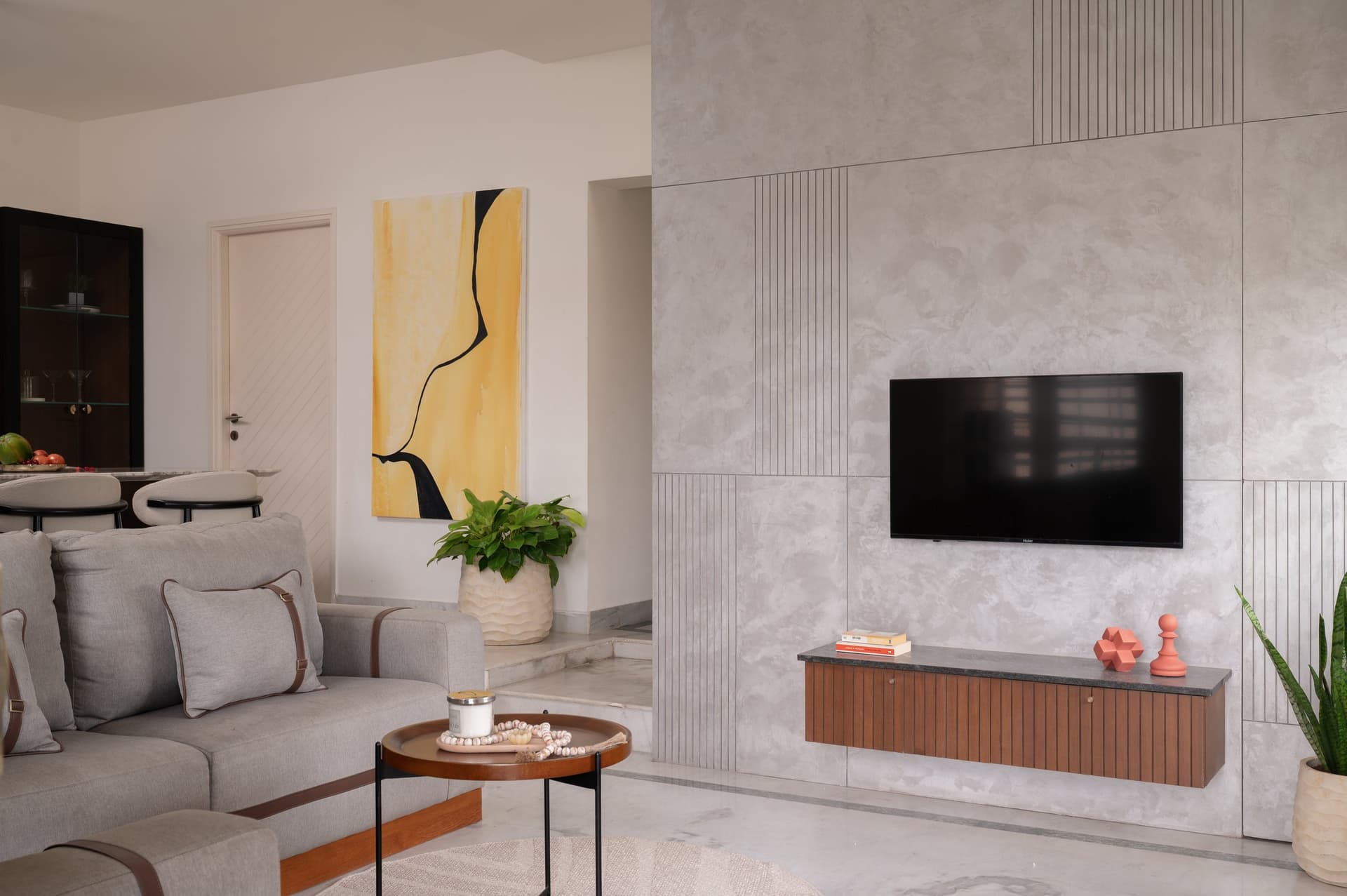 The living-room television wall in a concrete-toned finish, scored with vertical grooves that draw the eye toward the screen