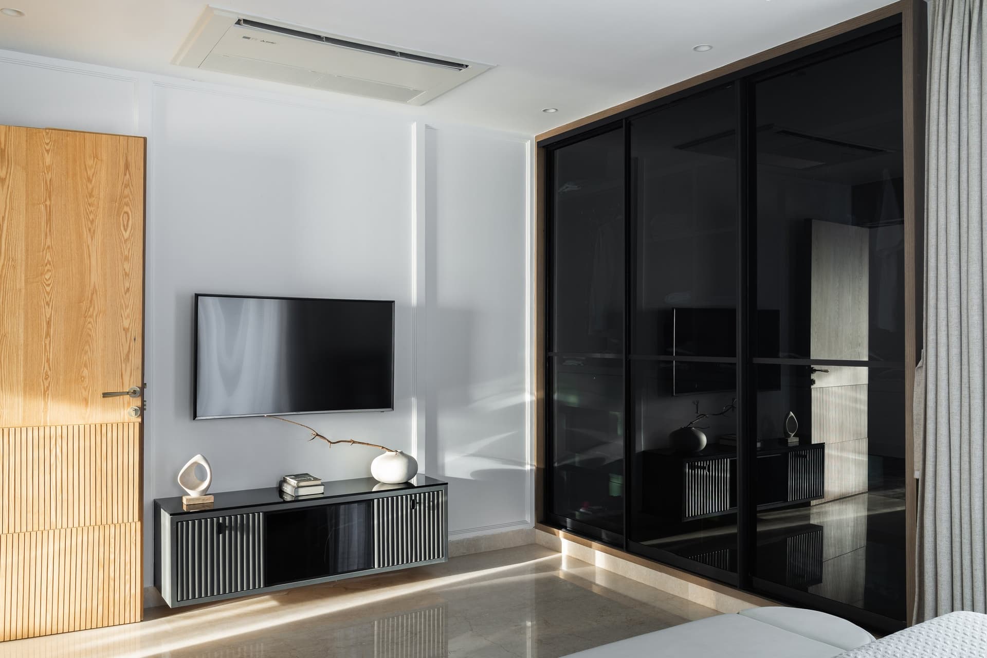 Opposite the bed, a fluted media console and a dark-tinted glass wardrobe extend the room's perceived volume