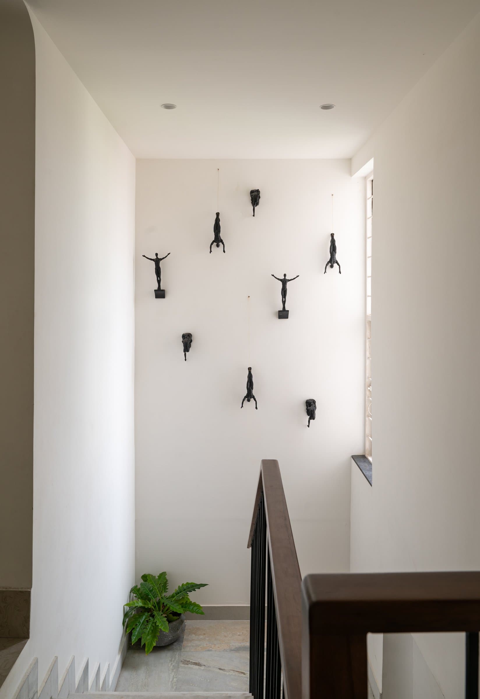 The stairwell, where small bronze figures scale the white wall in a loose, choreographed climb