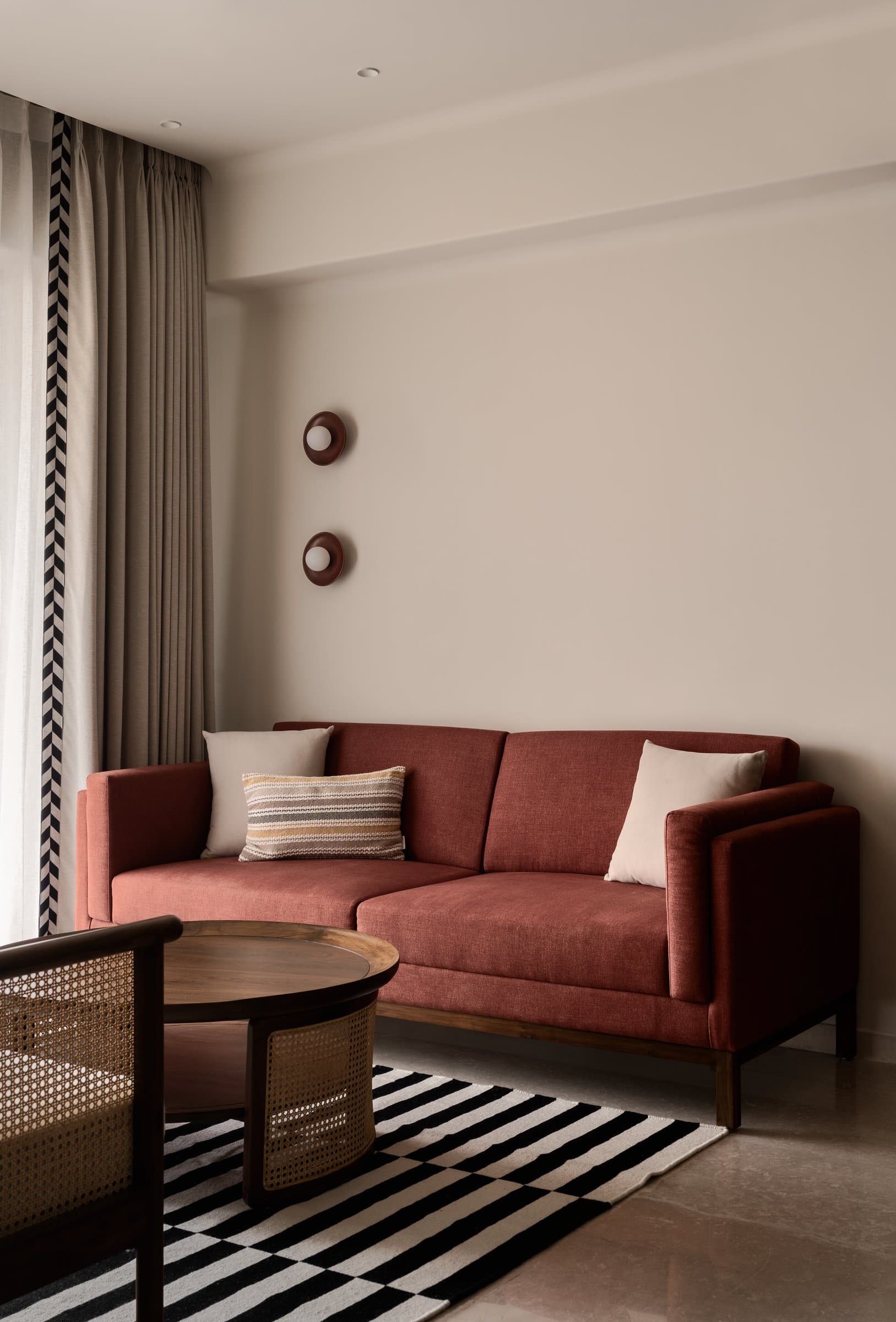 A terracotta-toned sofa introduces the home's warmest note, anchored by a striped rug and disc-shaped wall sconces
