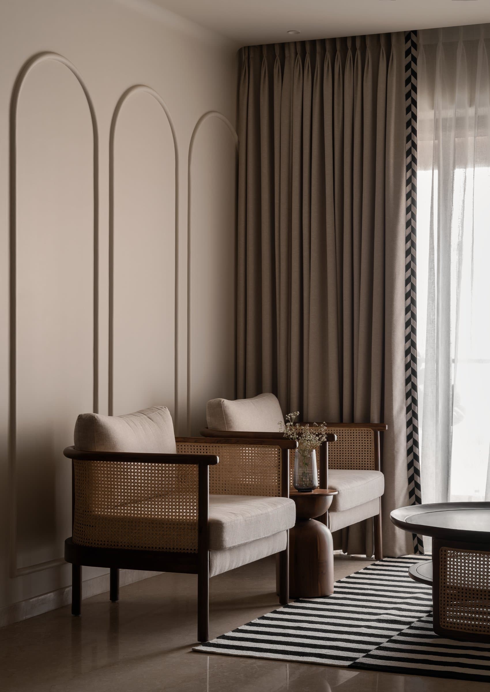 The living room, where slim arched wall mouldings and cane-and-wood armchairs hold a calibrated conversation with chevron-trimmed sheers