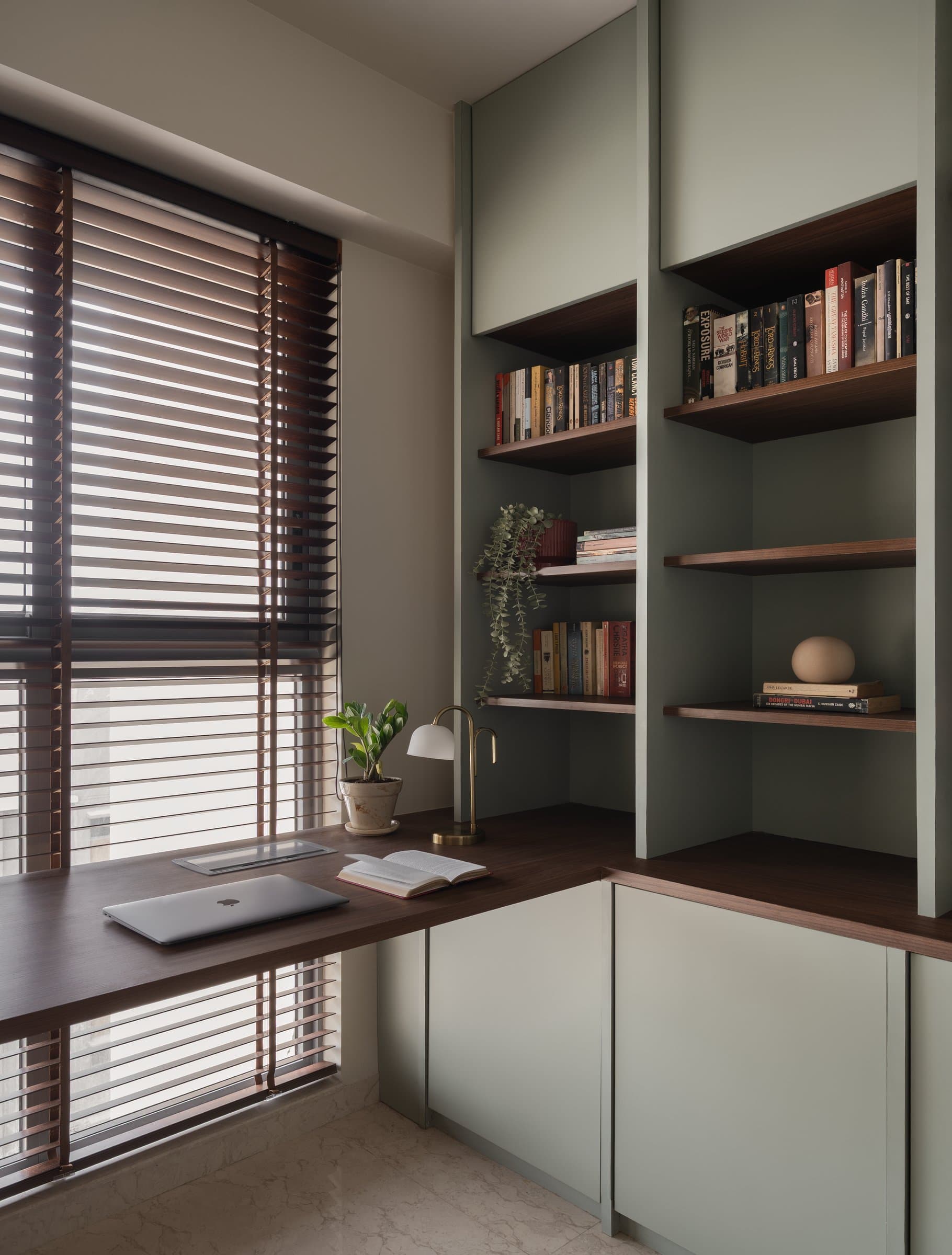 The home's study, where walnut joinery meets sage cabinetry and timbered Venetian blinds throw striped light across the floor