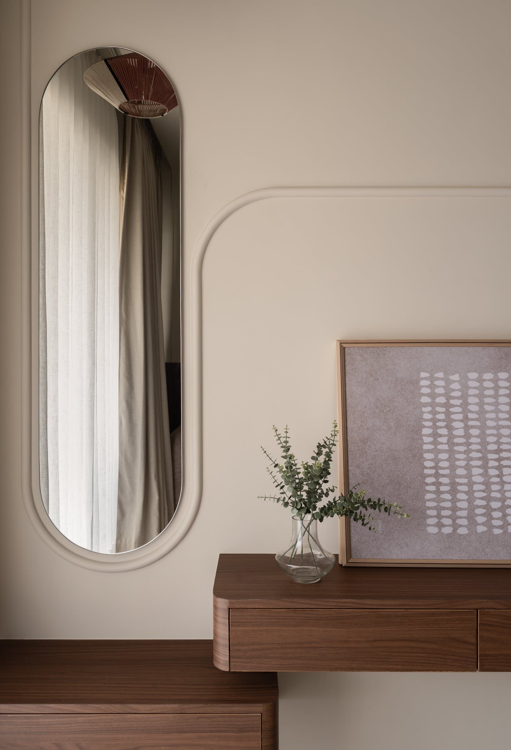 A dressing vignette pairs an oval mirror set into a rounded plaster reveal with a softened walnut console