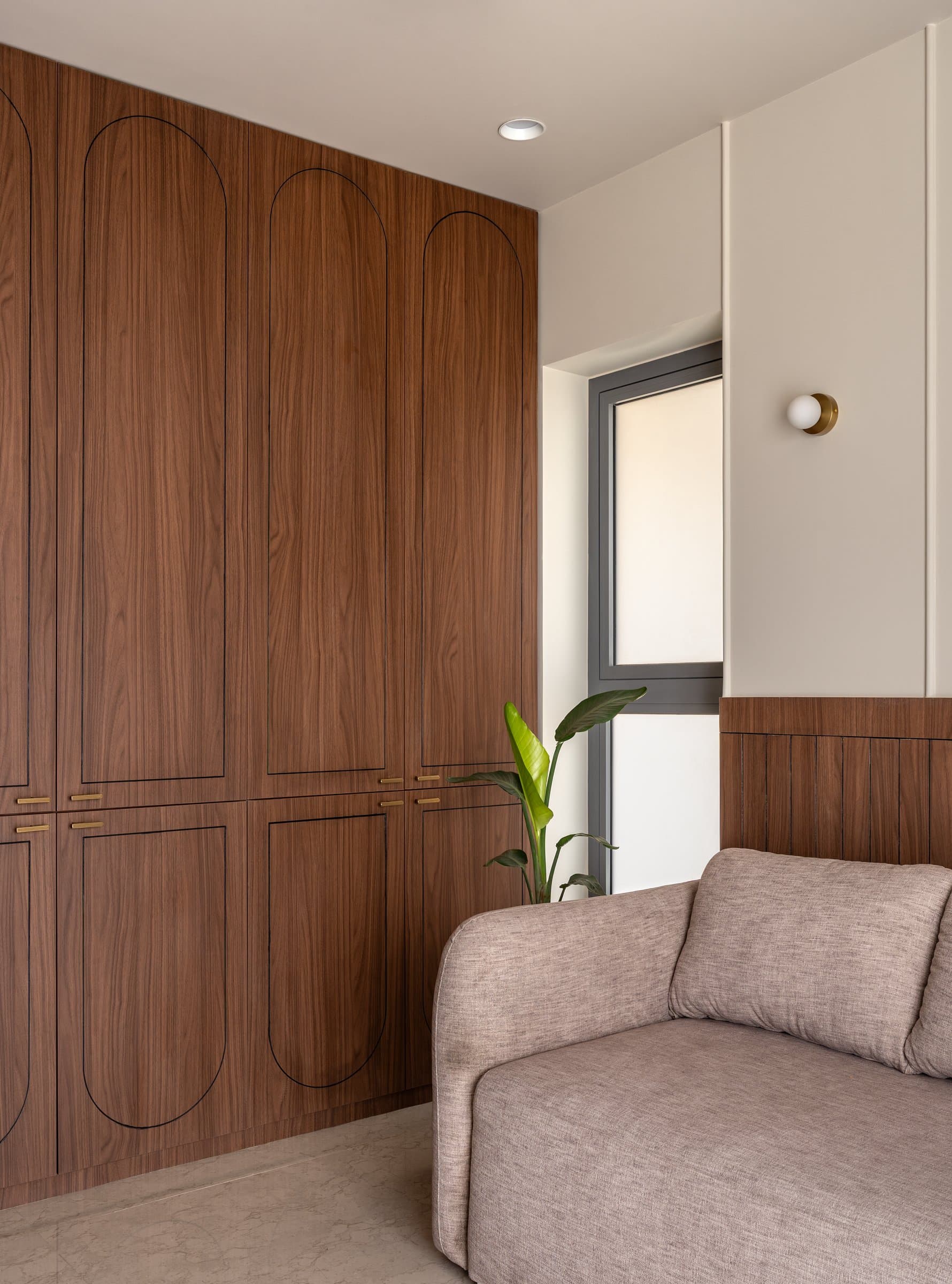 In the second bedroom, full-height walnut wardrobes inscribed with slim arched grooves carry the foyer's cane motif into a quieter line drawing