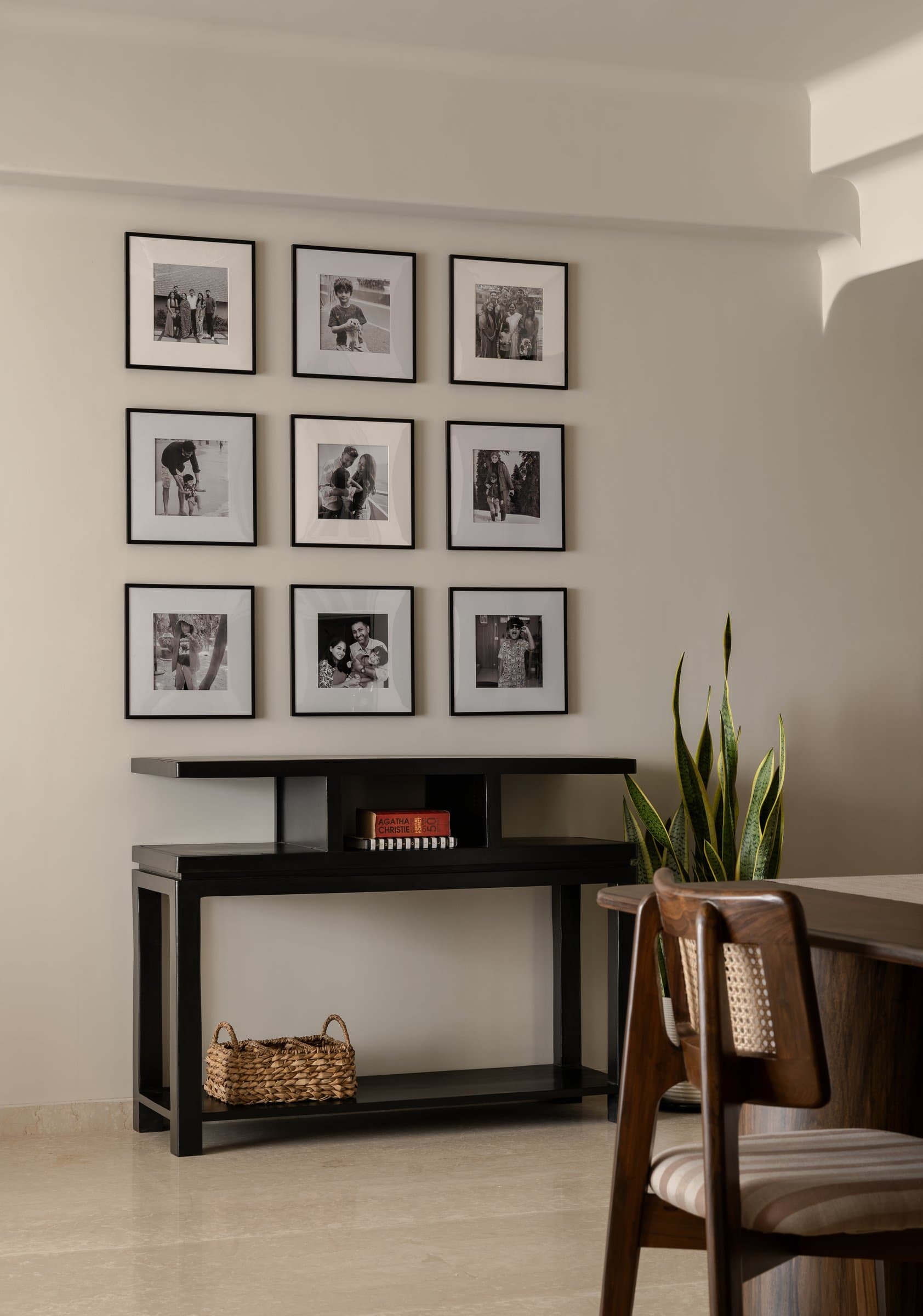 Beside the dining zone, a grid of nine family photographs above a slim black console layers memory into the design discipline