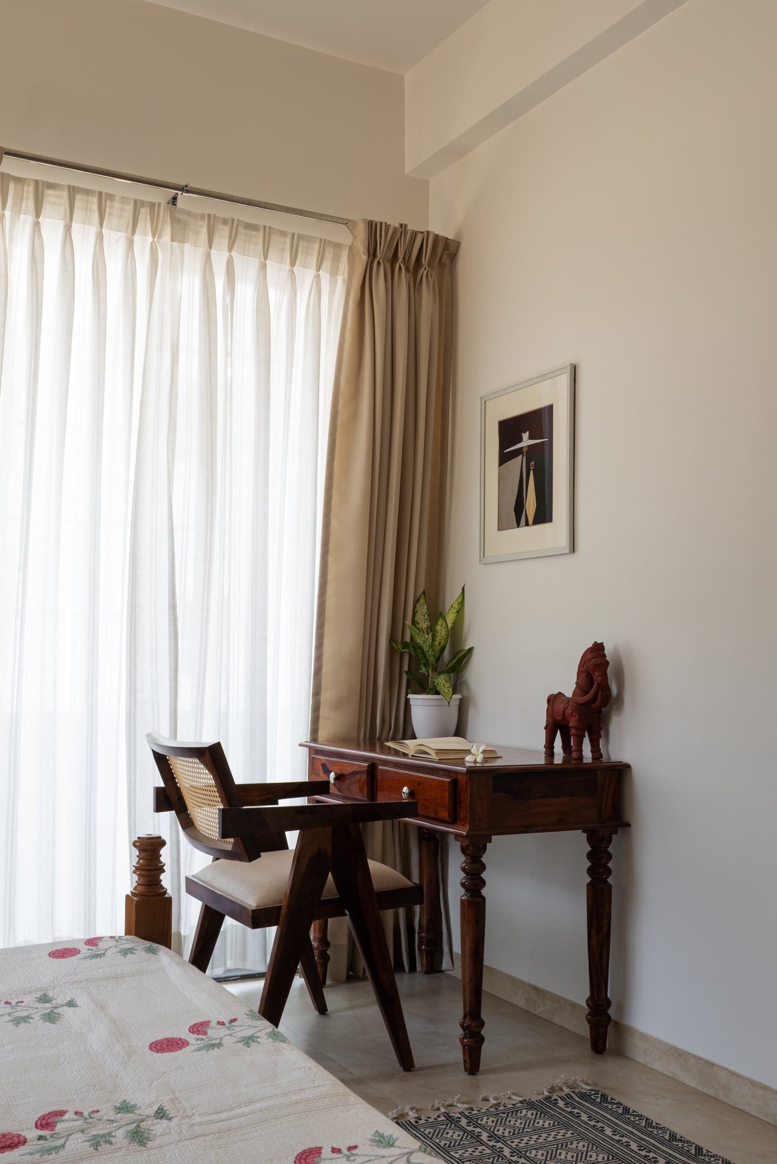 A writing corner within the same bedroom, where a caned chair drawn from the Chandigarh institutional vocabulary meets a turned-leg desk