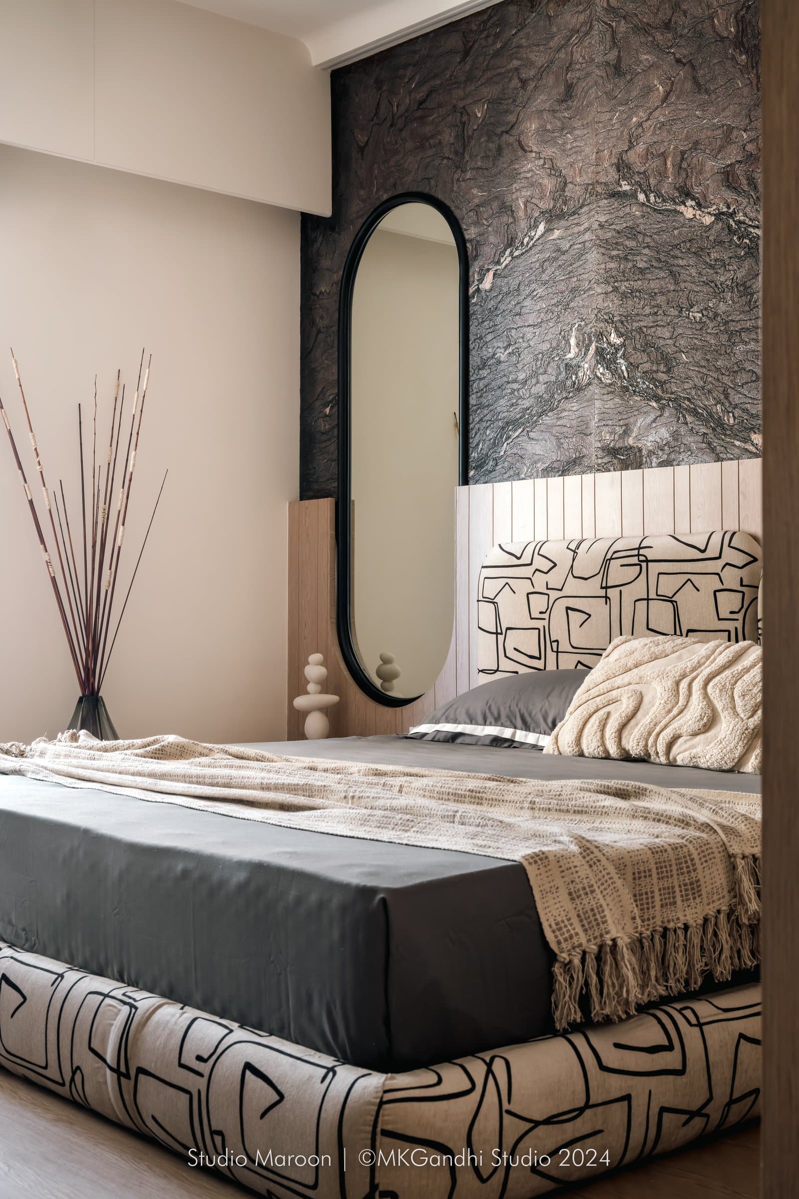 The master bedroom organised around a wall of figured dark stone and a tall oval mirror