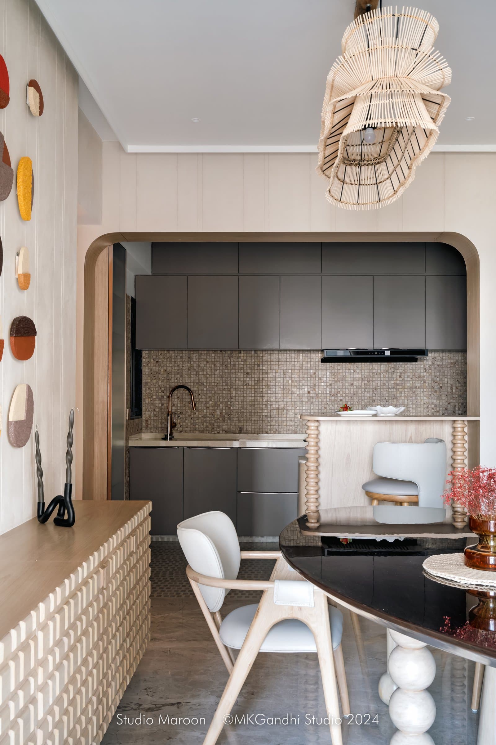The kitchen behind a softly arched opening, with a sculptural rattan pendant suspended above the dining table