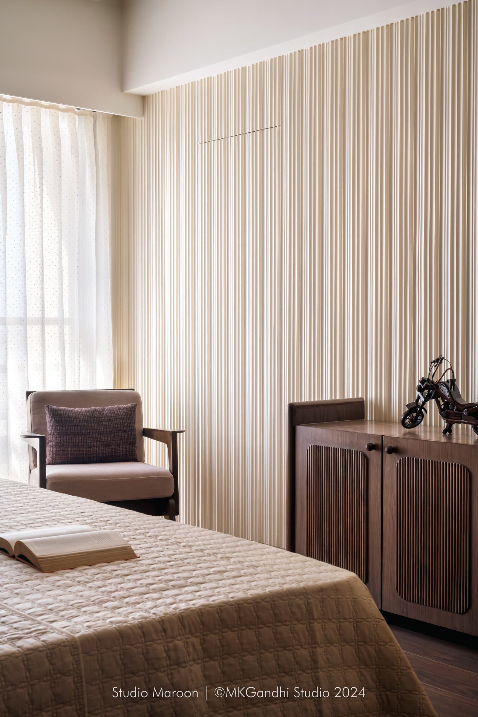 A third bedroom, where reeded walls meet warm flooring and a dusty pink linen armchair