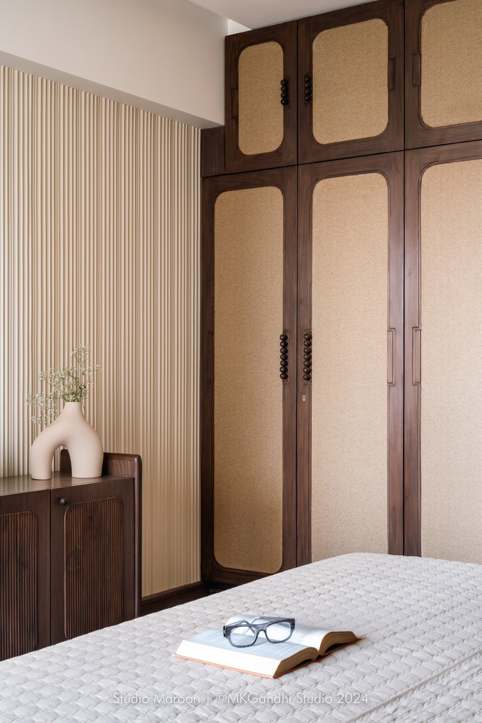 The wardrobe wall in dark wood and cane, set against a fluted cream reeded wall