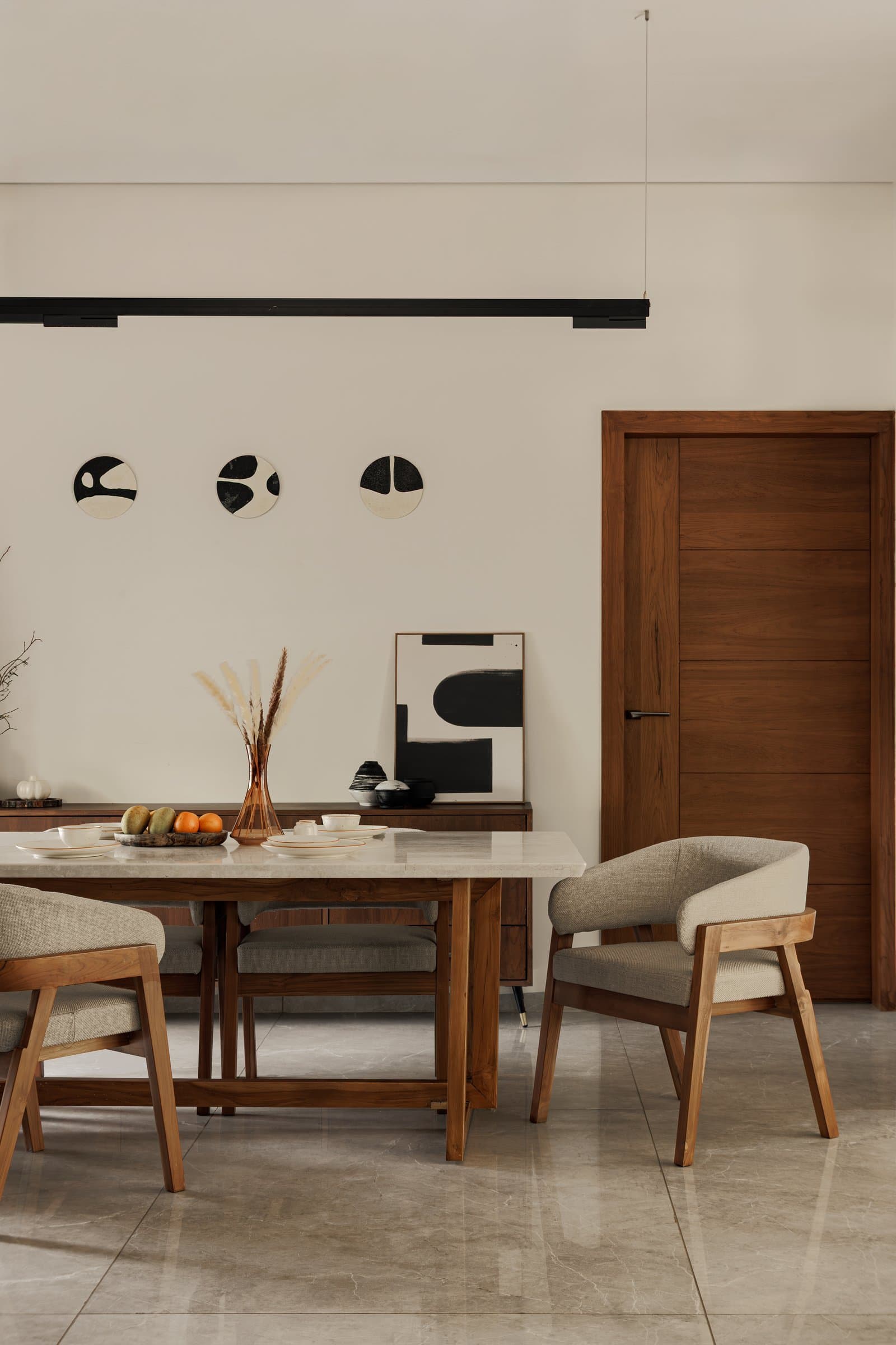 The dining room, a wooden trestle table with a pale stone top set against a quiet wall of three small ceramic discs