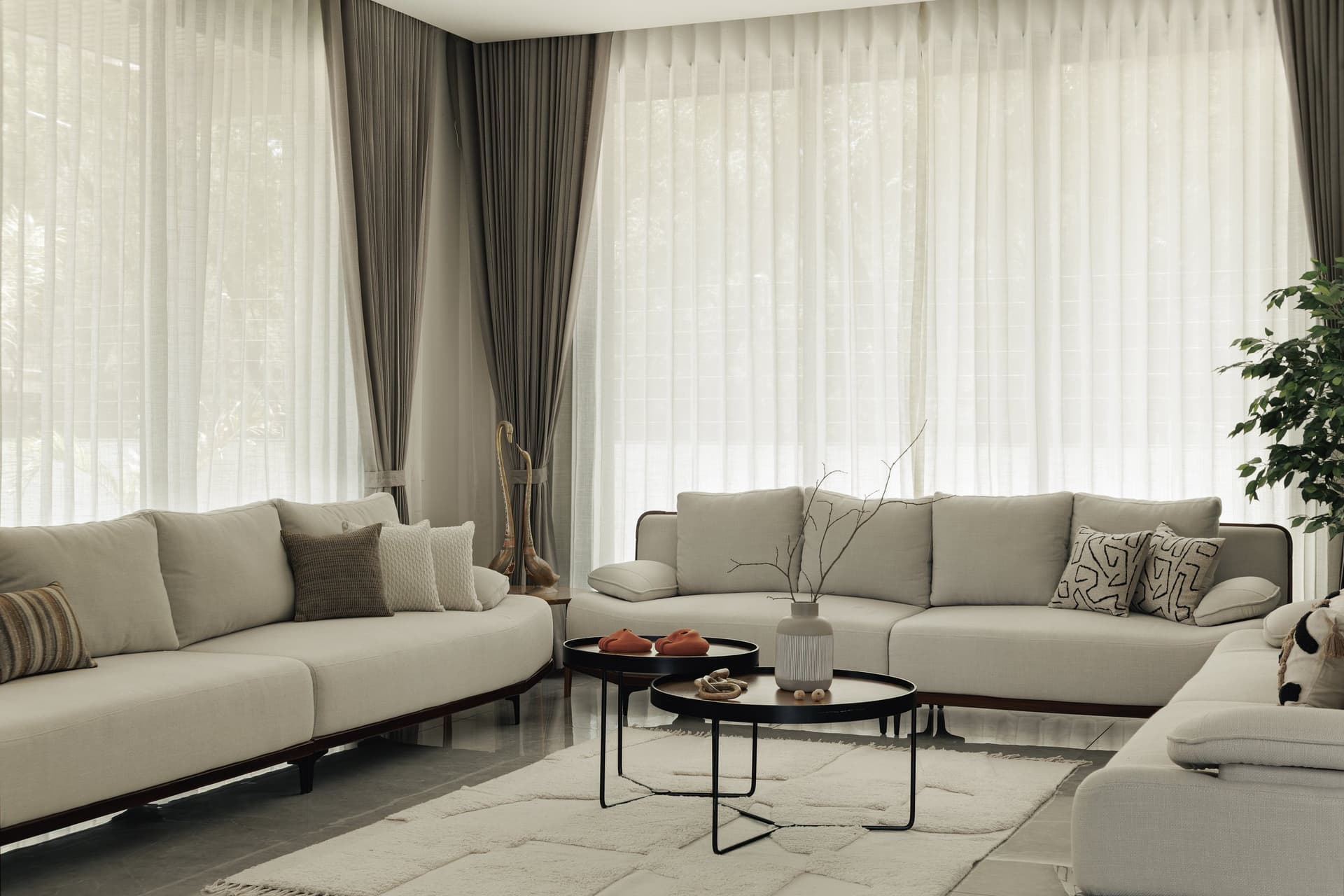 The principal living room, where curved oatmeal sofas and full-height sheer drapery hold the home’s social register in a single neutral key