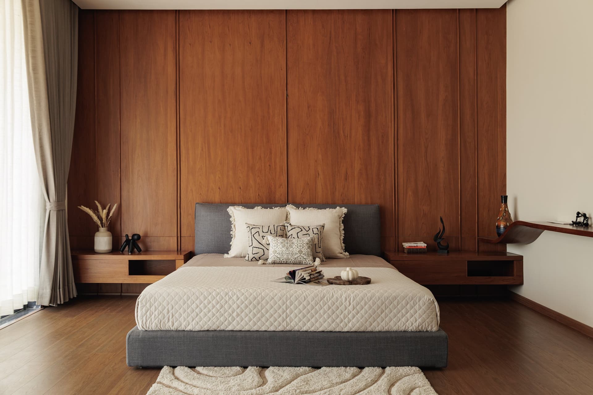 The master bedroom, organised around a tall panelled wood wall and a low grey upholstered bed