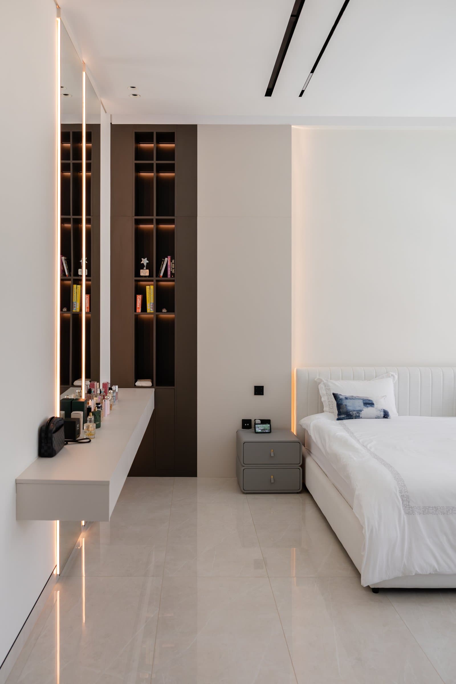 The master bedroom, where a fluted upholstered headboard sits opposite a floating vanity and warm linear cove lighting