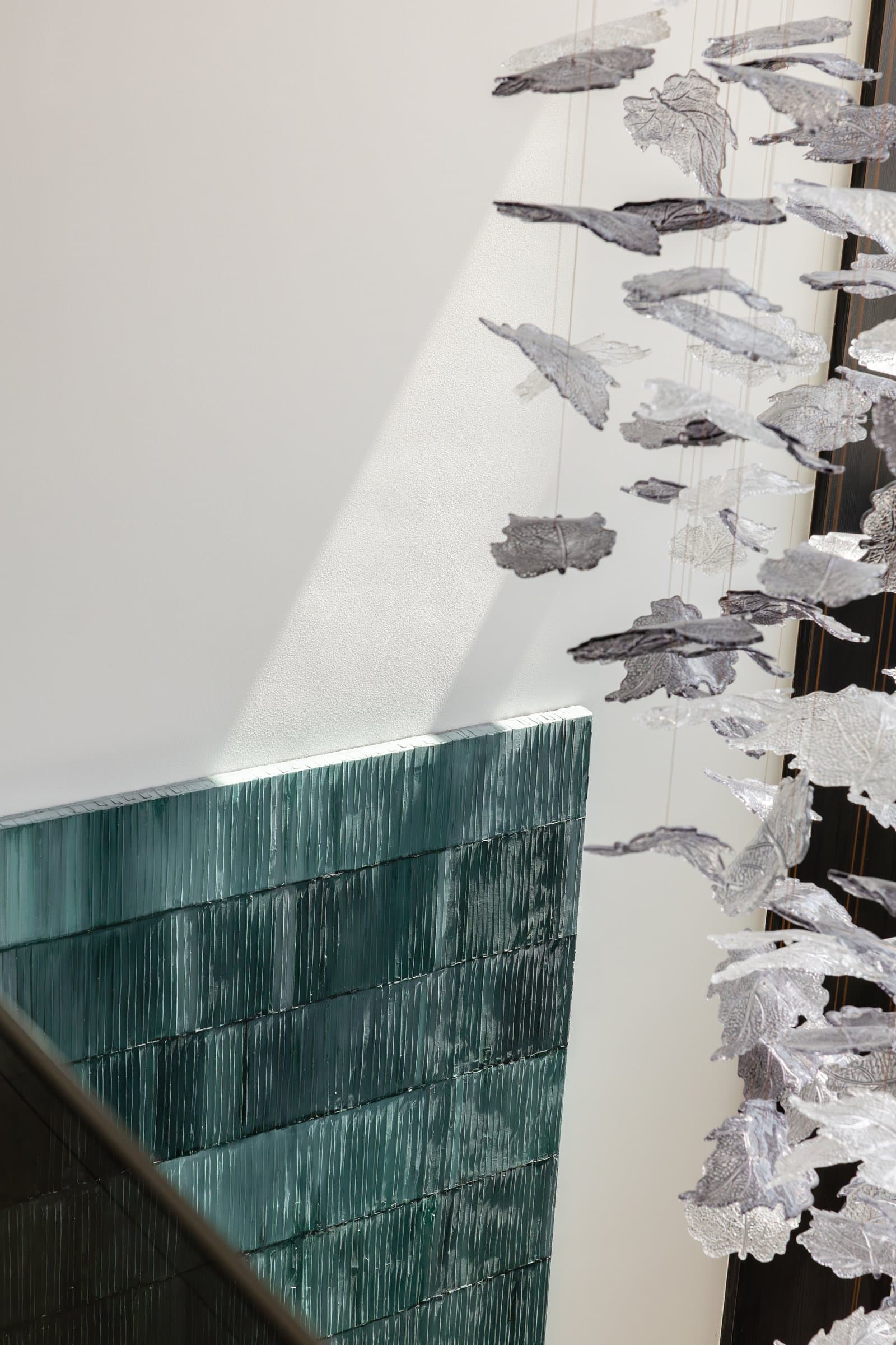The suspended installation seen from the stair, where a green textured glass wall and cascading pale forms anchor the home's central void