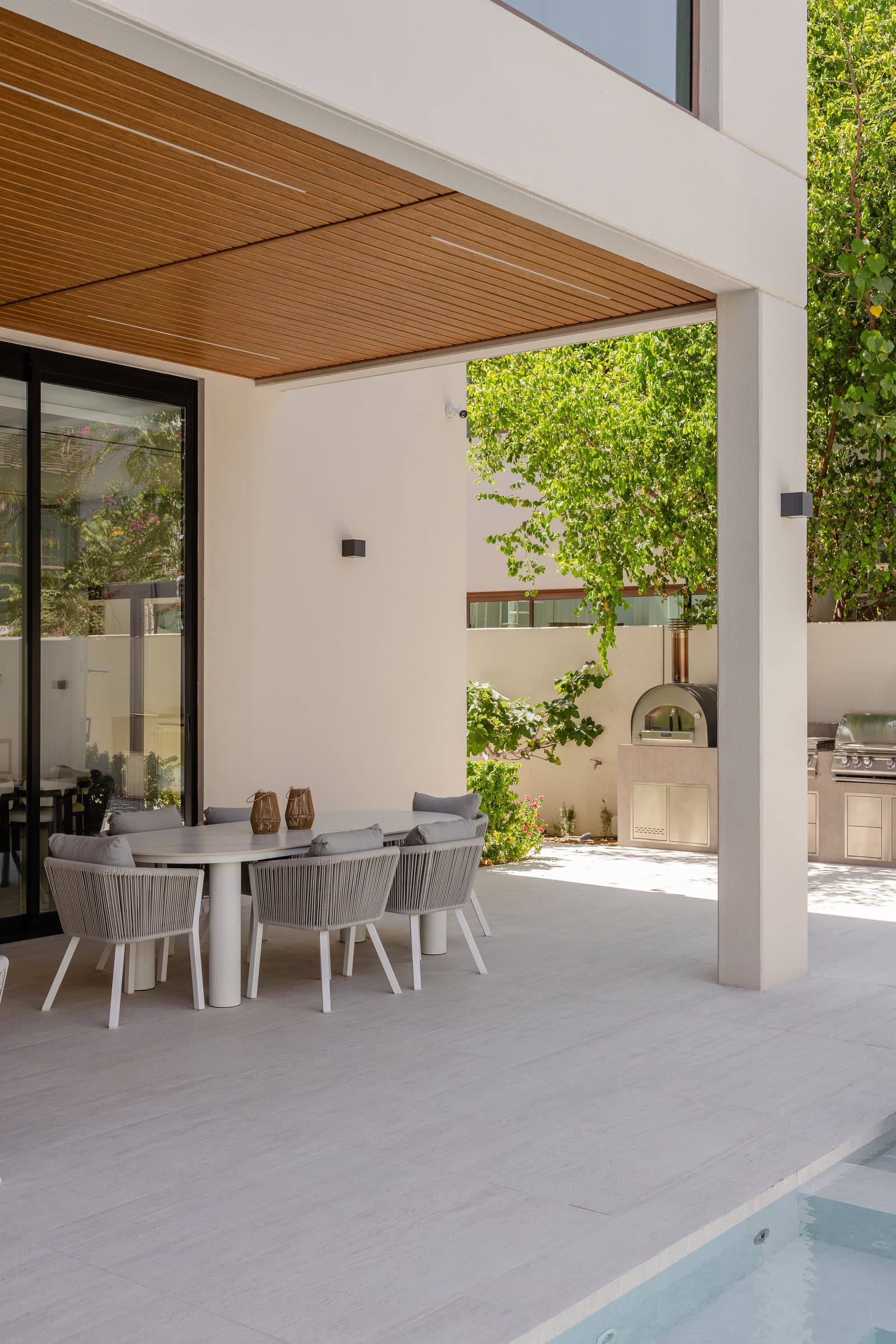 The covered terrace, where a warm wood-slatted ceiling tempers the pale stone deck and frames the pool beyond