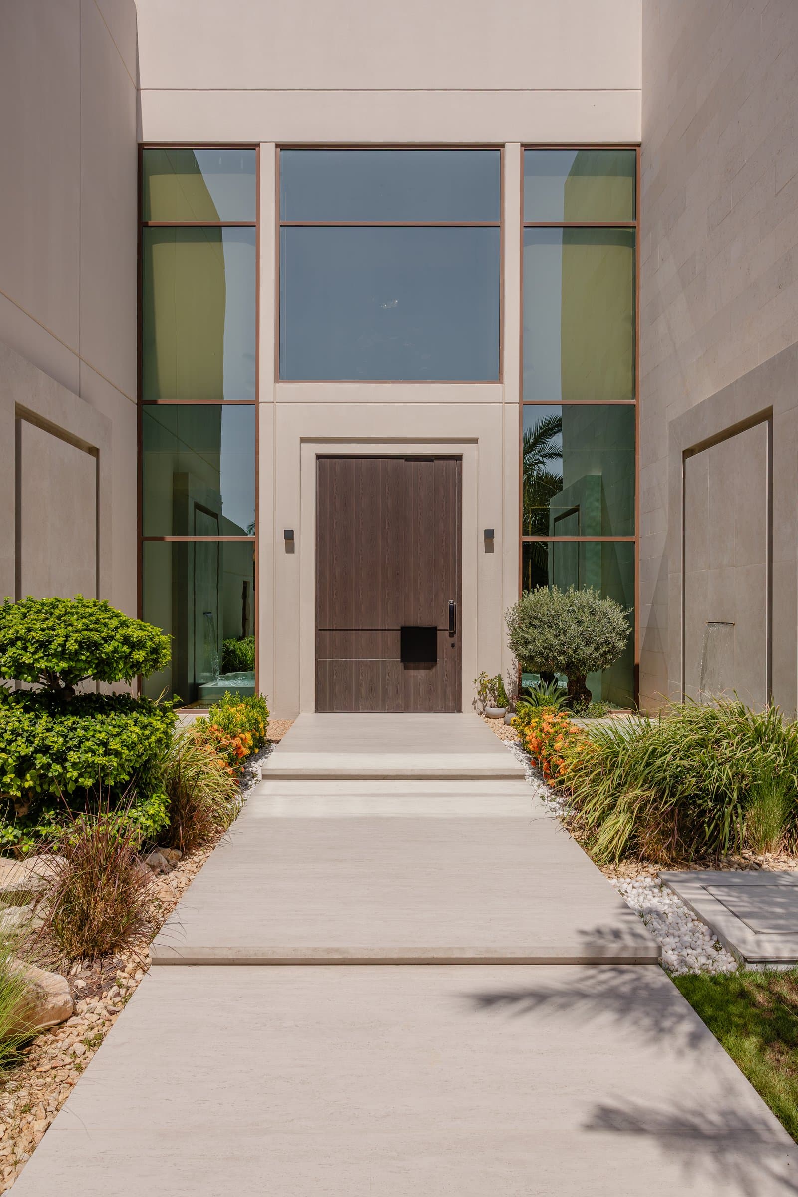 The entry approach, where a dark wood pivot door and tall glazed screen establish the home's restrained architectural language