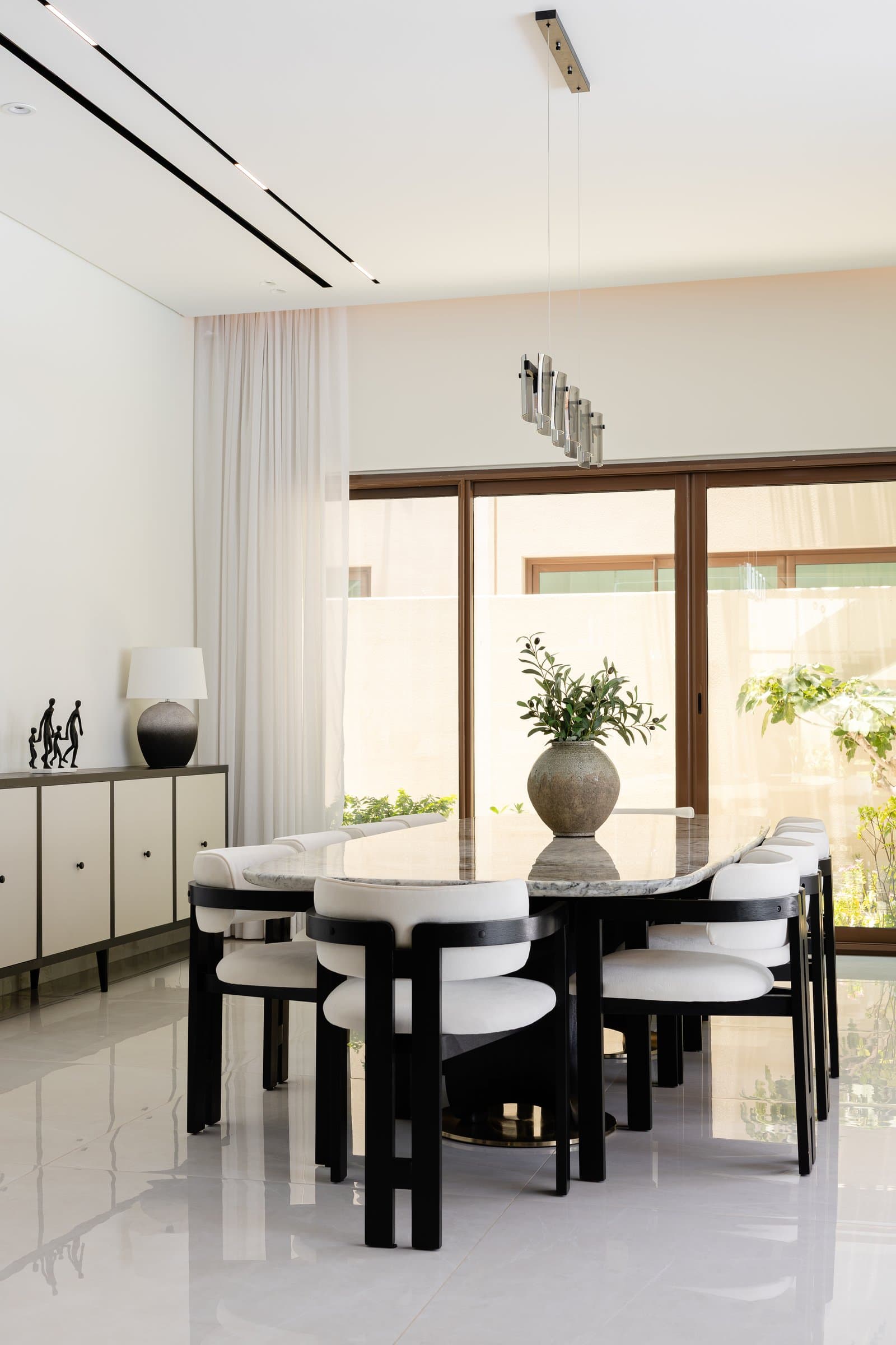 The dining room, where a veined stone-topped table and black-framed chairs sit beneath a horizontal mirrored pendant