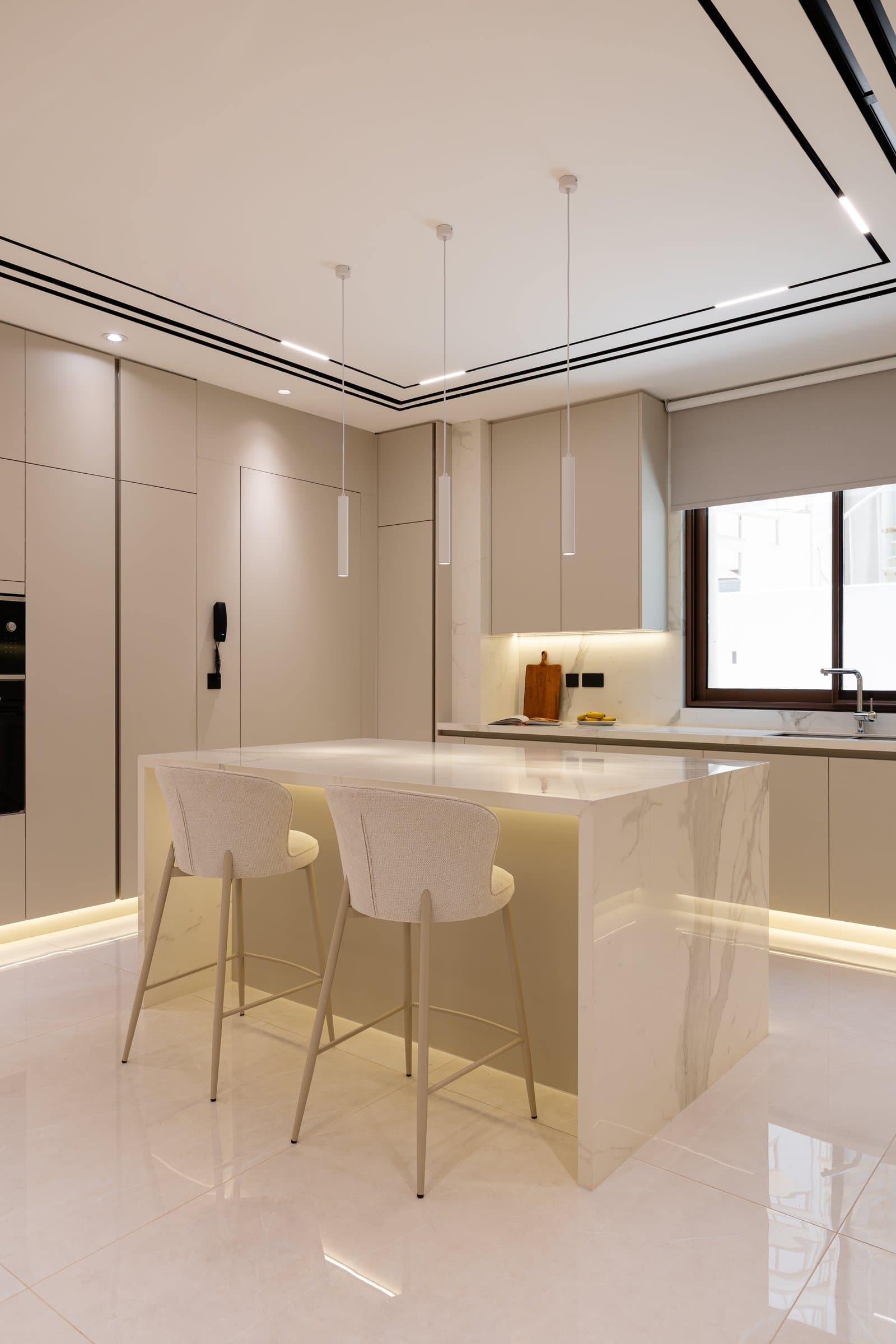 The kitchen, where a veined stone island and integrated cove lighting anchor a quiet palette of neutral cabinetry