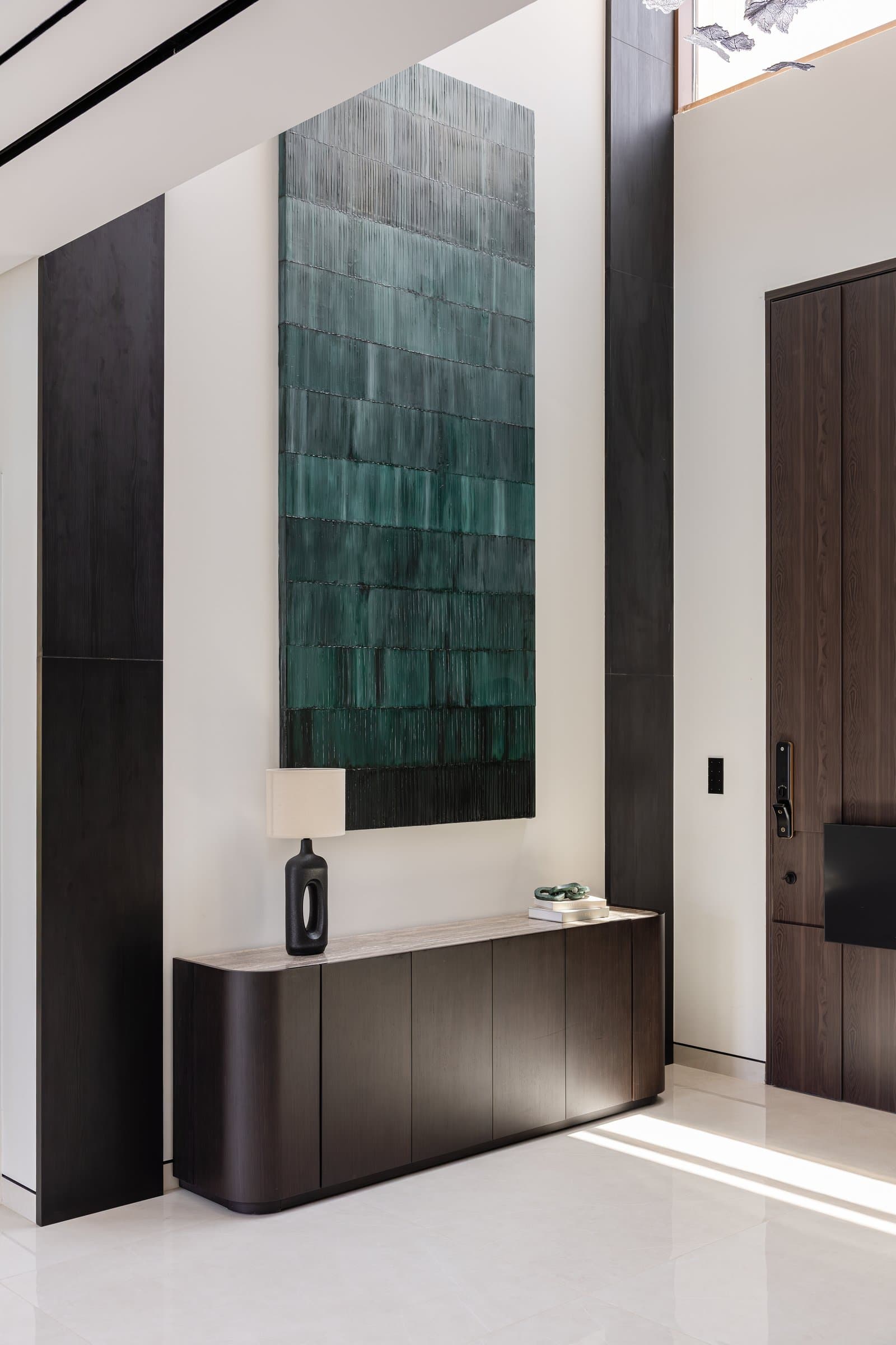 The foyer, where a graduated green artwork and dark vertical panels set the material grammar over a stone-topped console