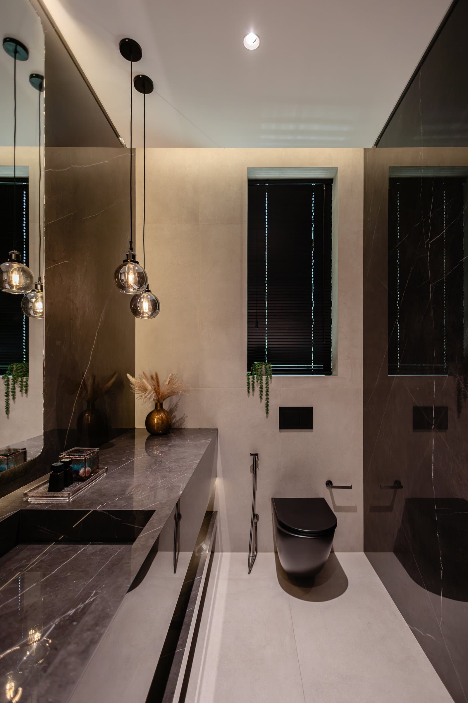 The powder room, where veined dark stone and smoked glass globe pendants compose a concentrated, moody interior